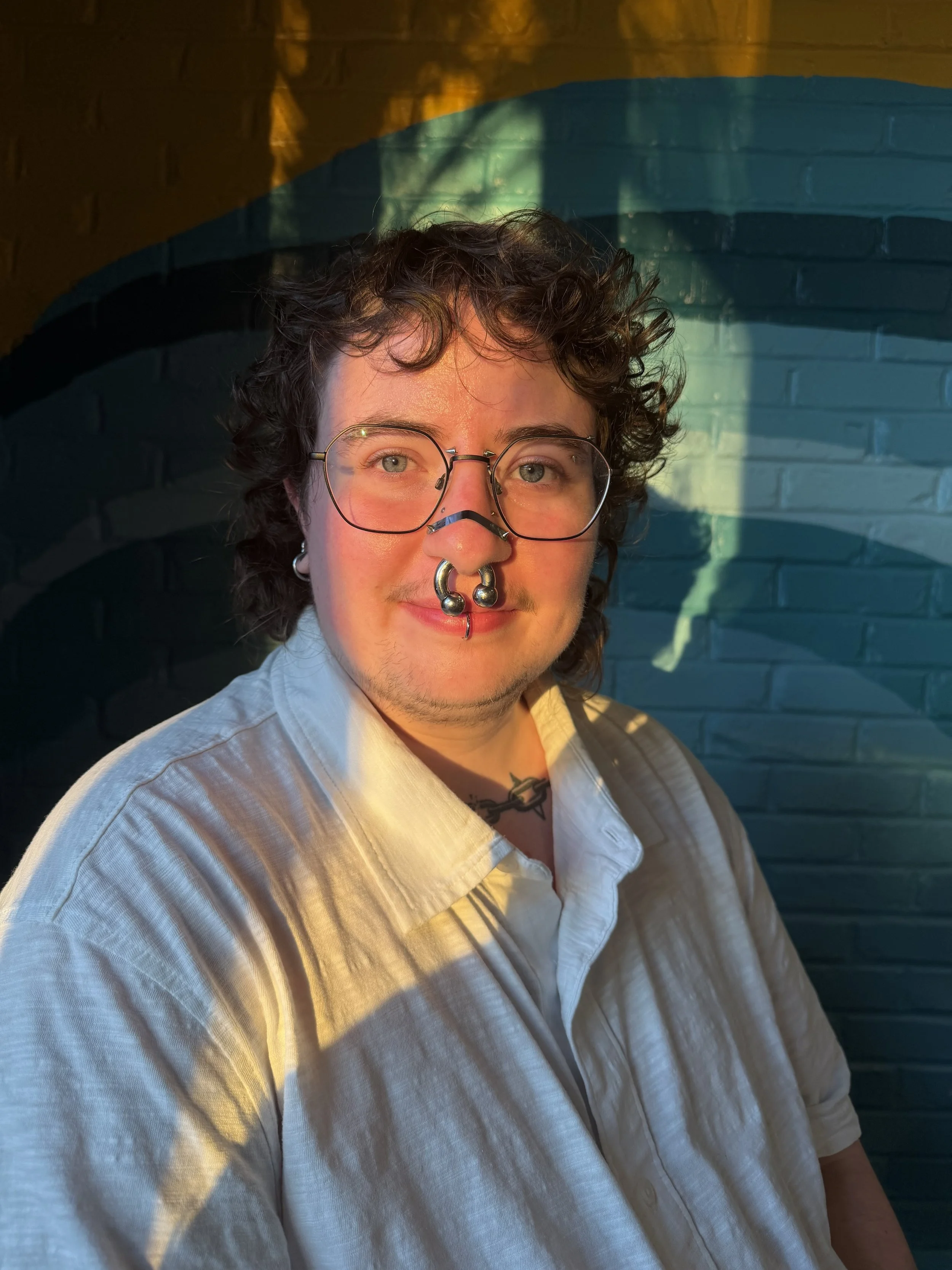 This is a photo of Kade, in a white shirt, wearing black glasses and smiling at the camera.