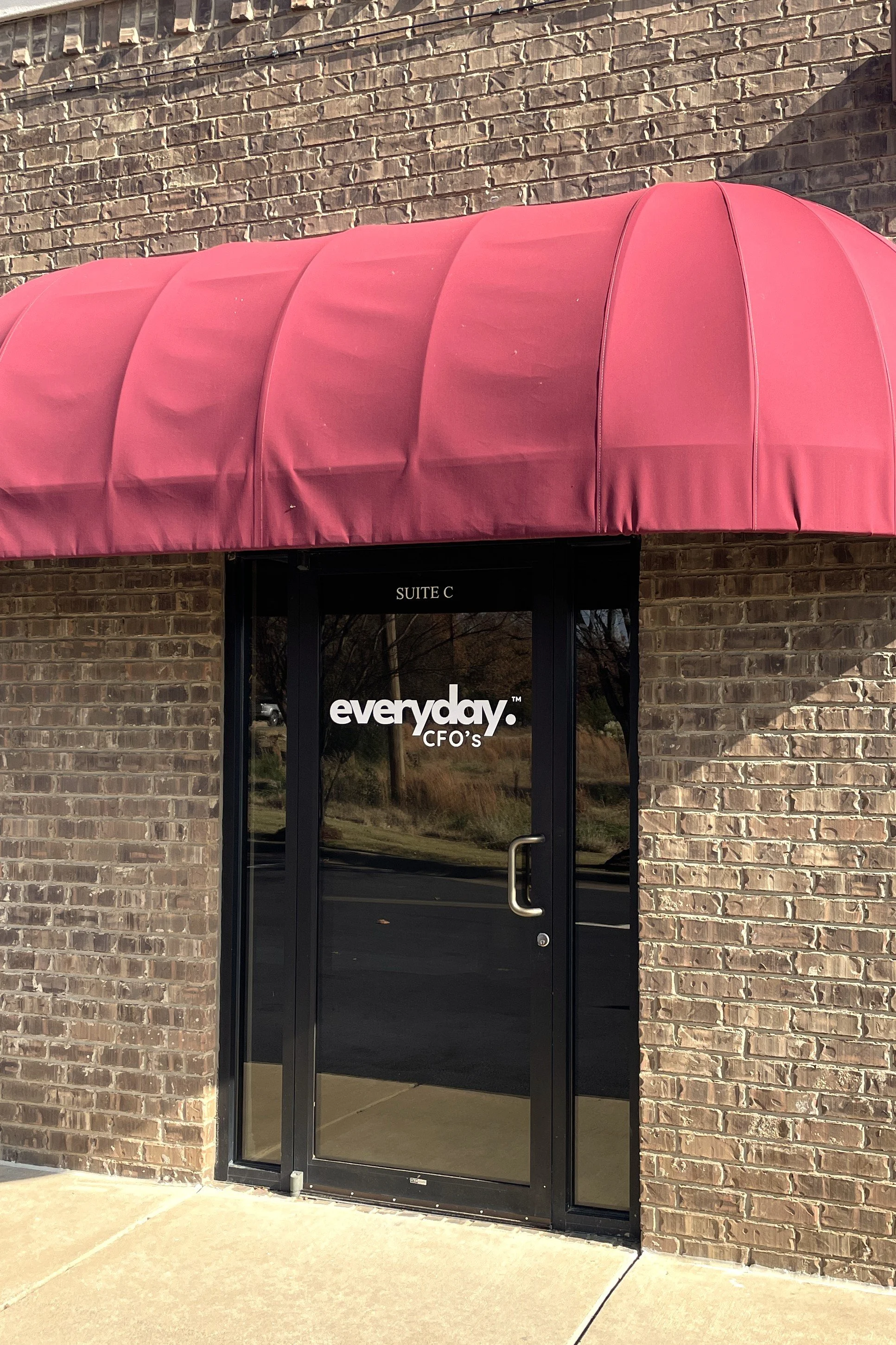 Red awning above a single glass front door on a tan brick building. The door has the logo Everyday CFO's on it.
