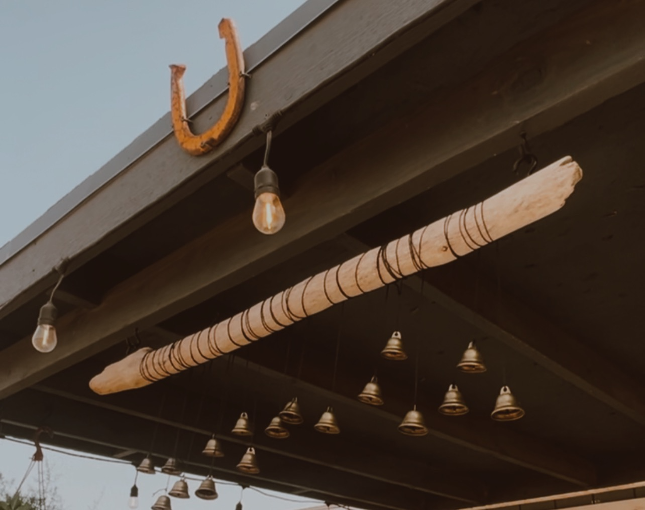 Decorative porch ceiling with string lights, a horseshoe on the edge, and a wooden bar with black wire wrapping.