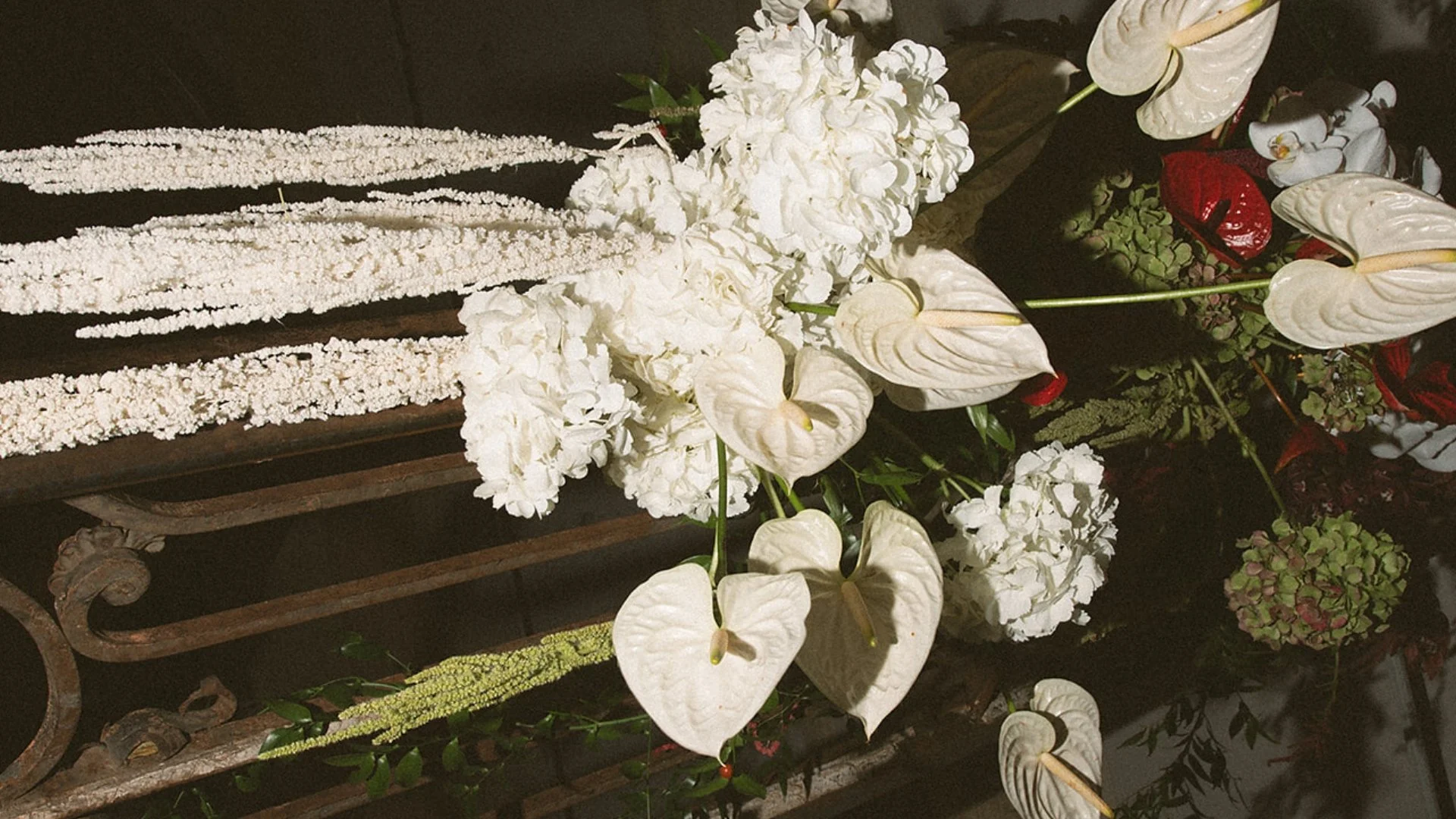 A floral arrangement on a vintage metal and wood cart, featuring white flowers including calla lilies and hydrangeas, with dark background.