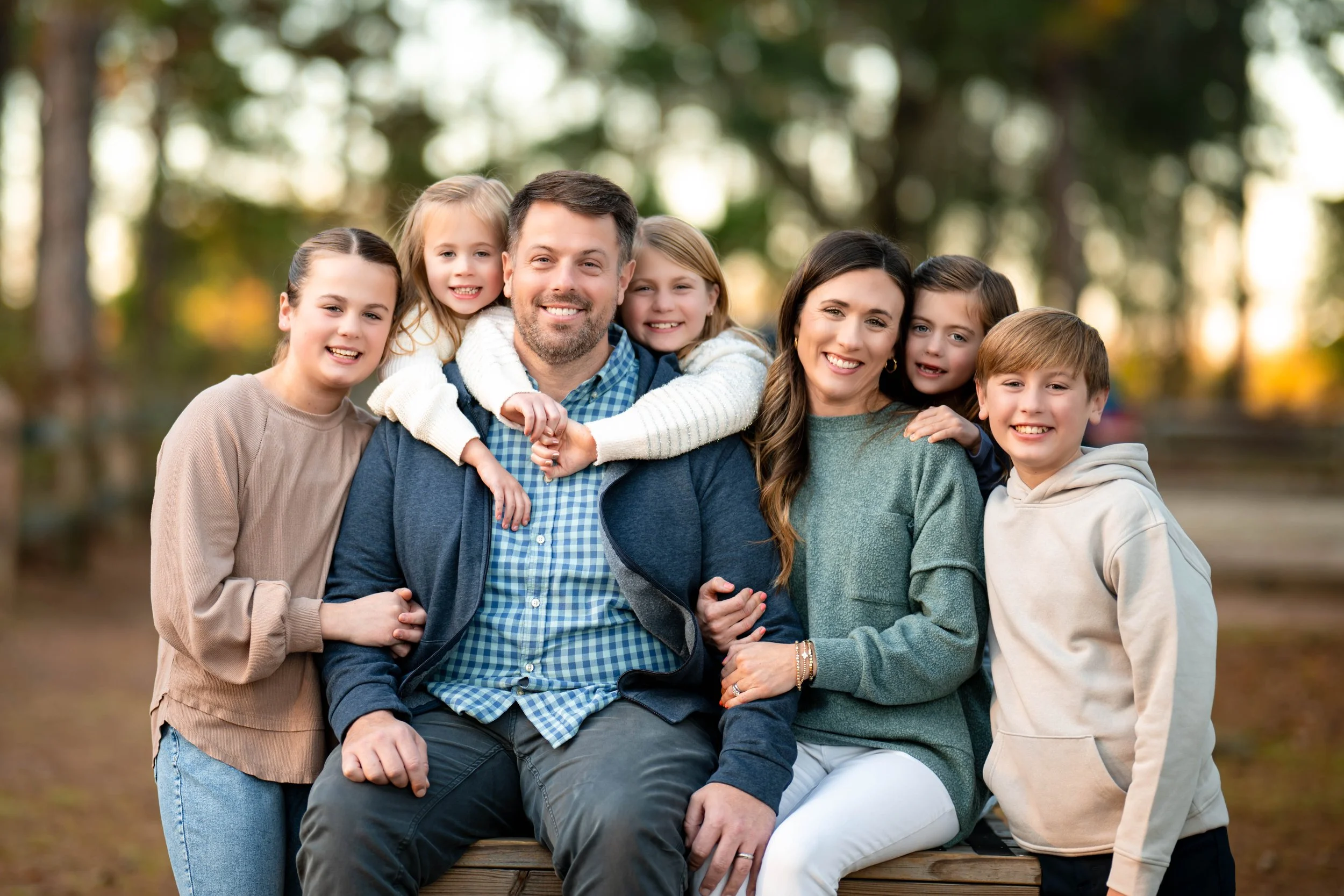 Family of seven posing outdoors in a park during autumn, with children and parents smiling.