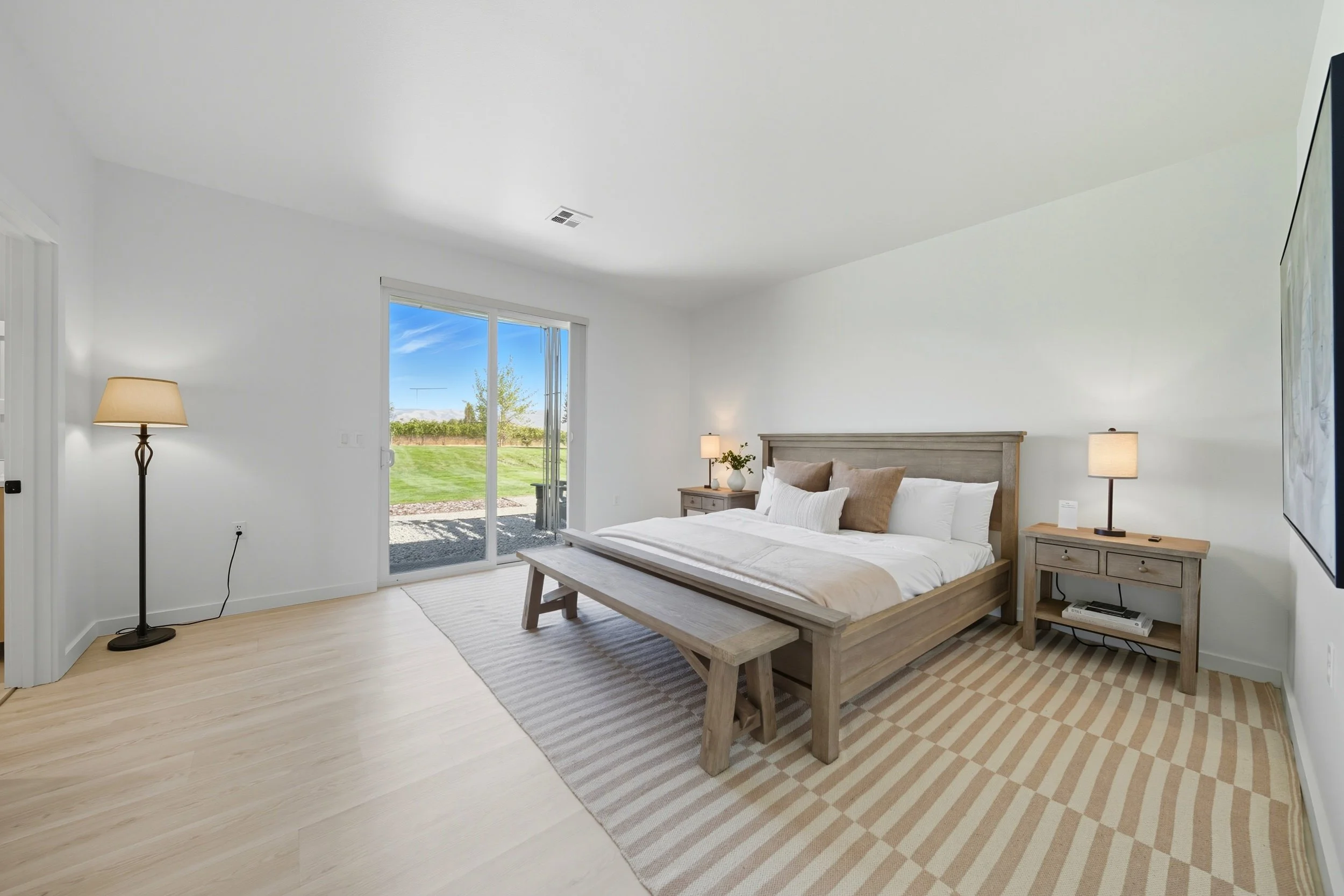 Bedroom with a wooden bed, two nightstands with lamps, a sliding glass door leading outside, and a view of the backyard.