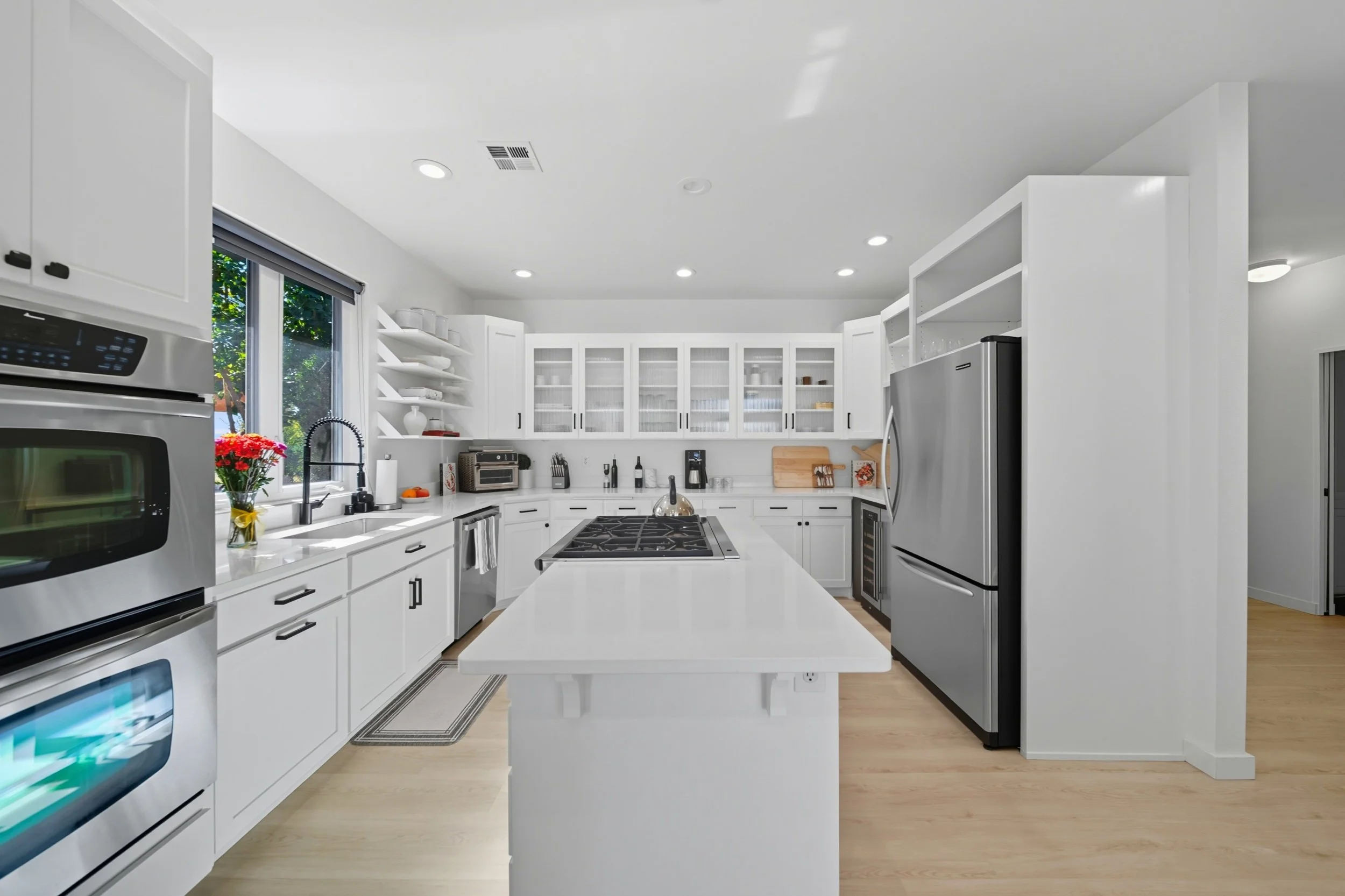 Bright, modern kitchen with white cabinets, stainless steel appliances, a central island, and a window with greenery outside.
