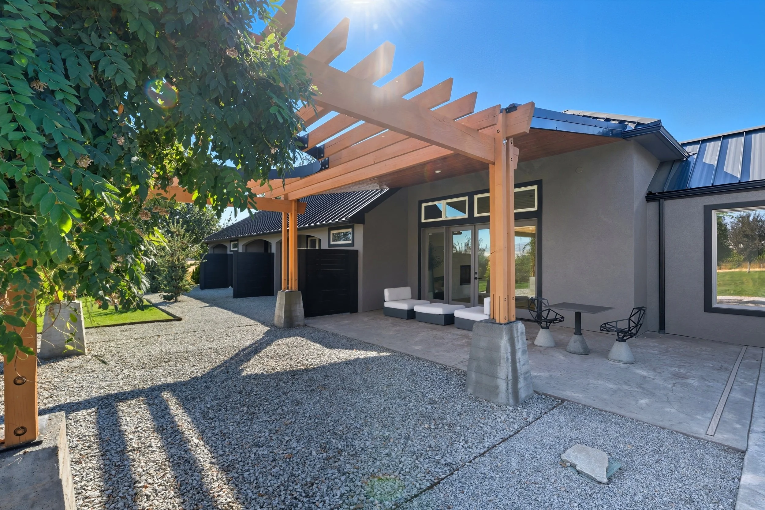 Modern backyard patio with outdoor seating, a pergola frame, and gravel and concrete ground surfaces.
