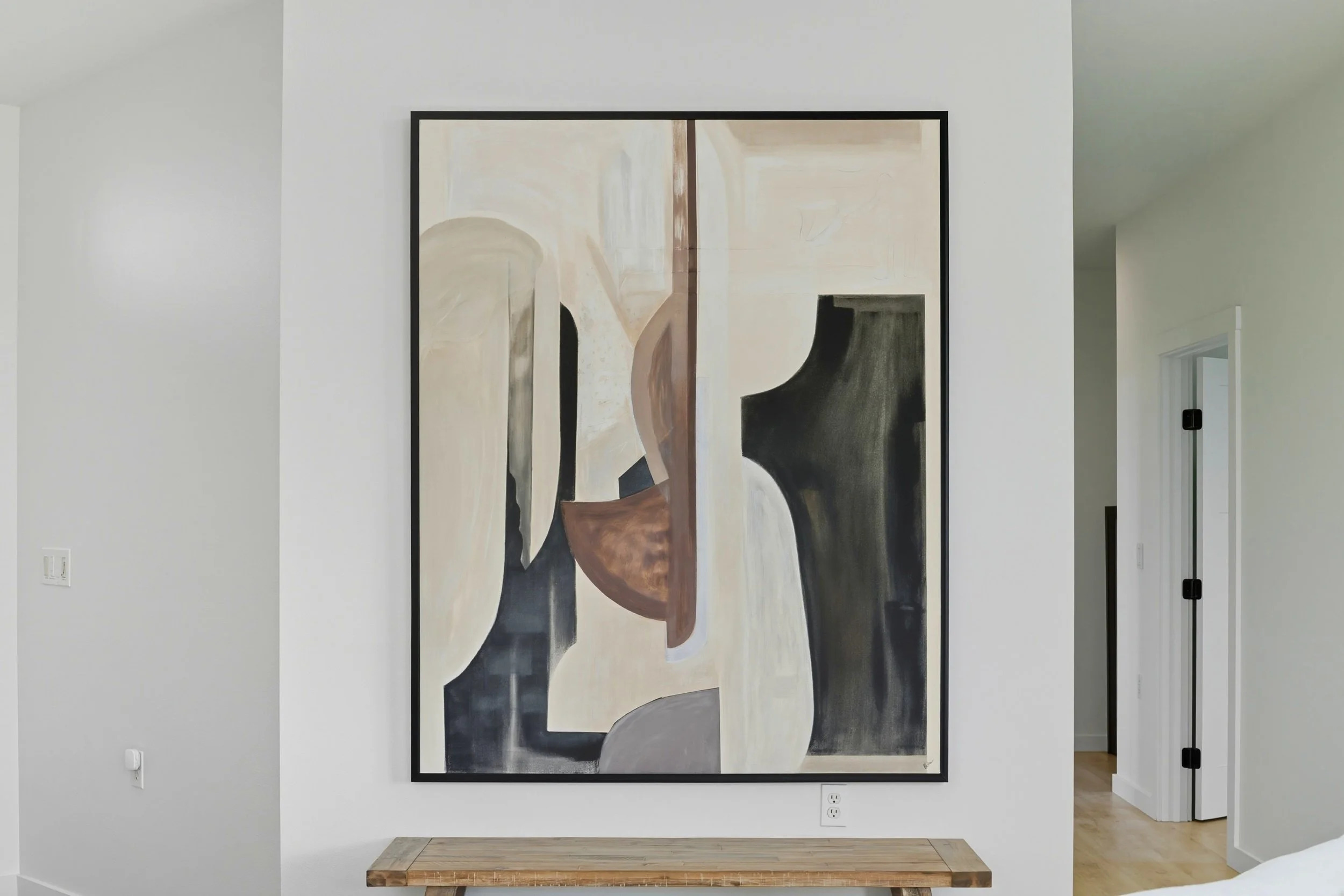 Abstract painting with geometric shapes and neutral colors hung on a white wall.