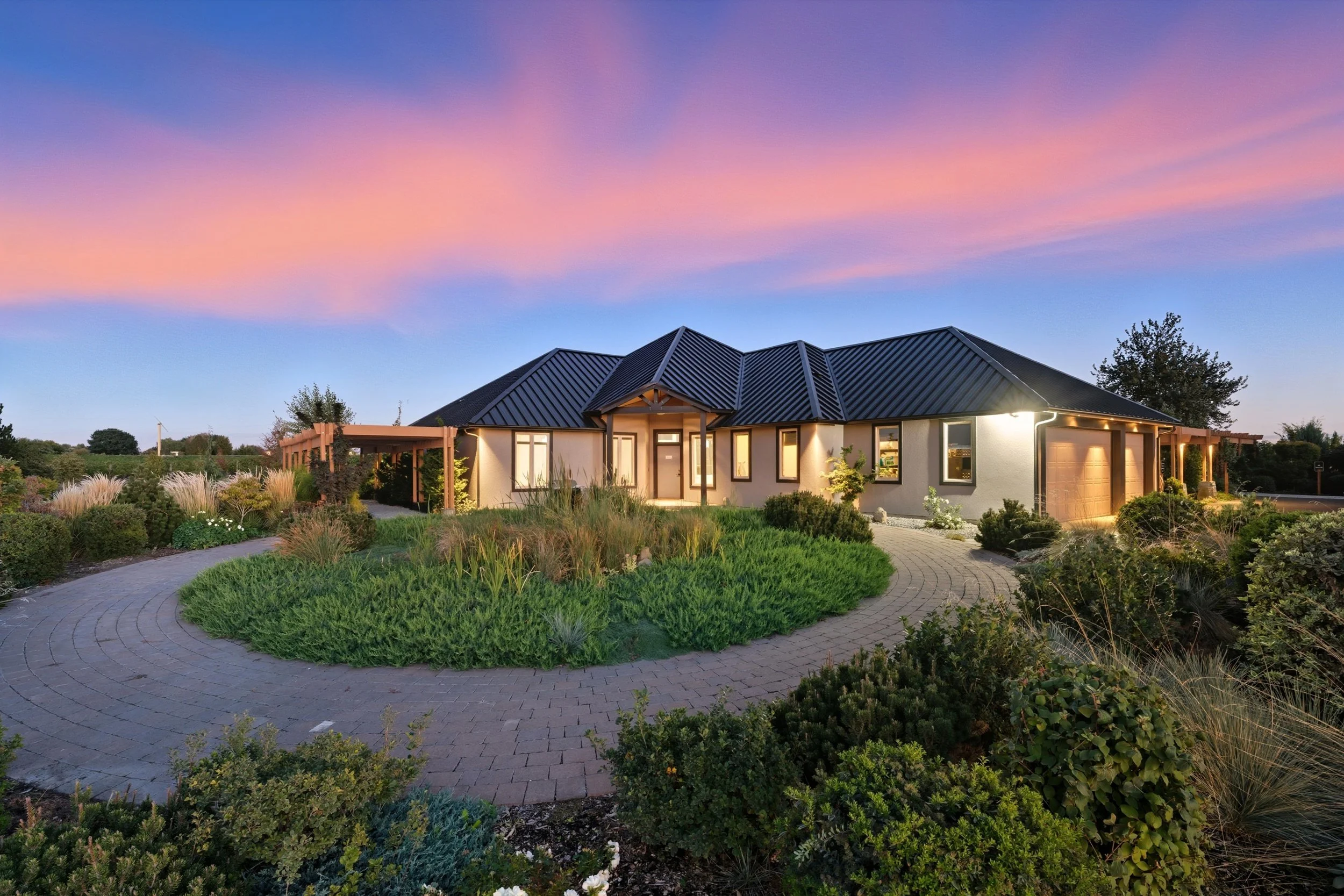 A modern house with a black metal roof, large windows, and a well-maintained garden during sunset.