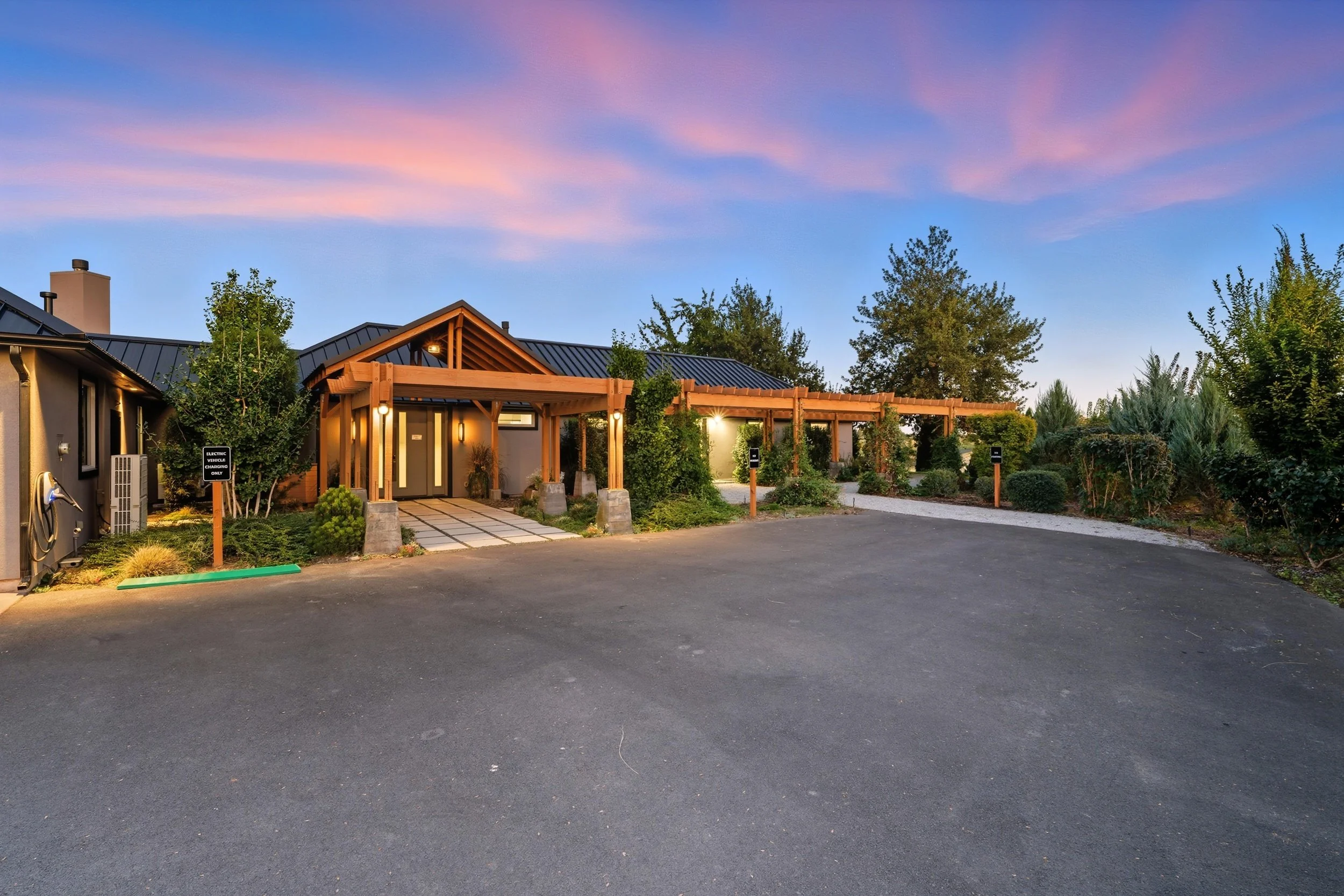 Modern residential building with wooden accents, landscaped greenery, and parking lot at twilight.