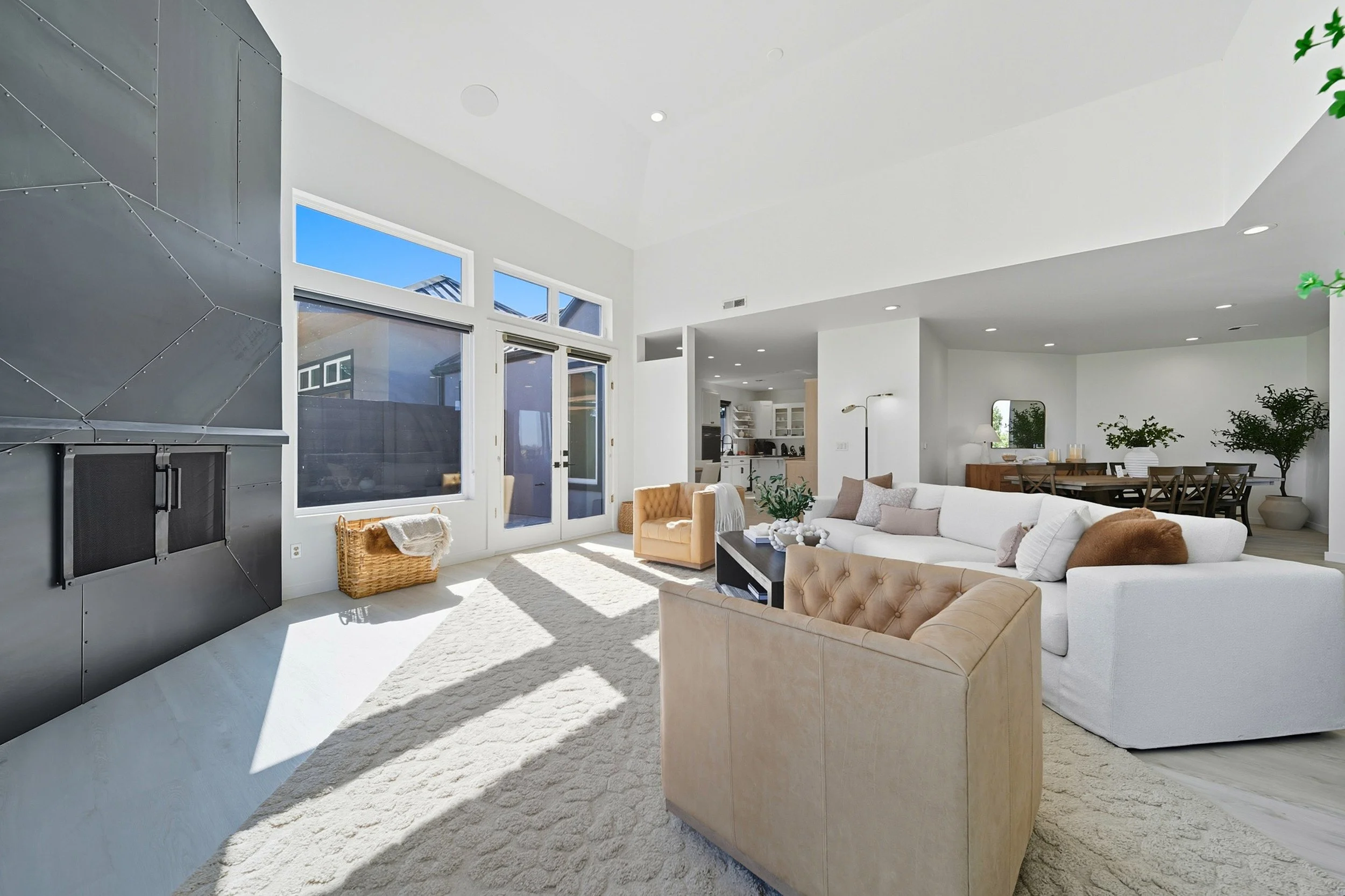 Bright living room with large windows, white walls, beige and white furniture, and a light-colored carpet.
