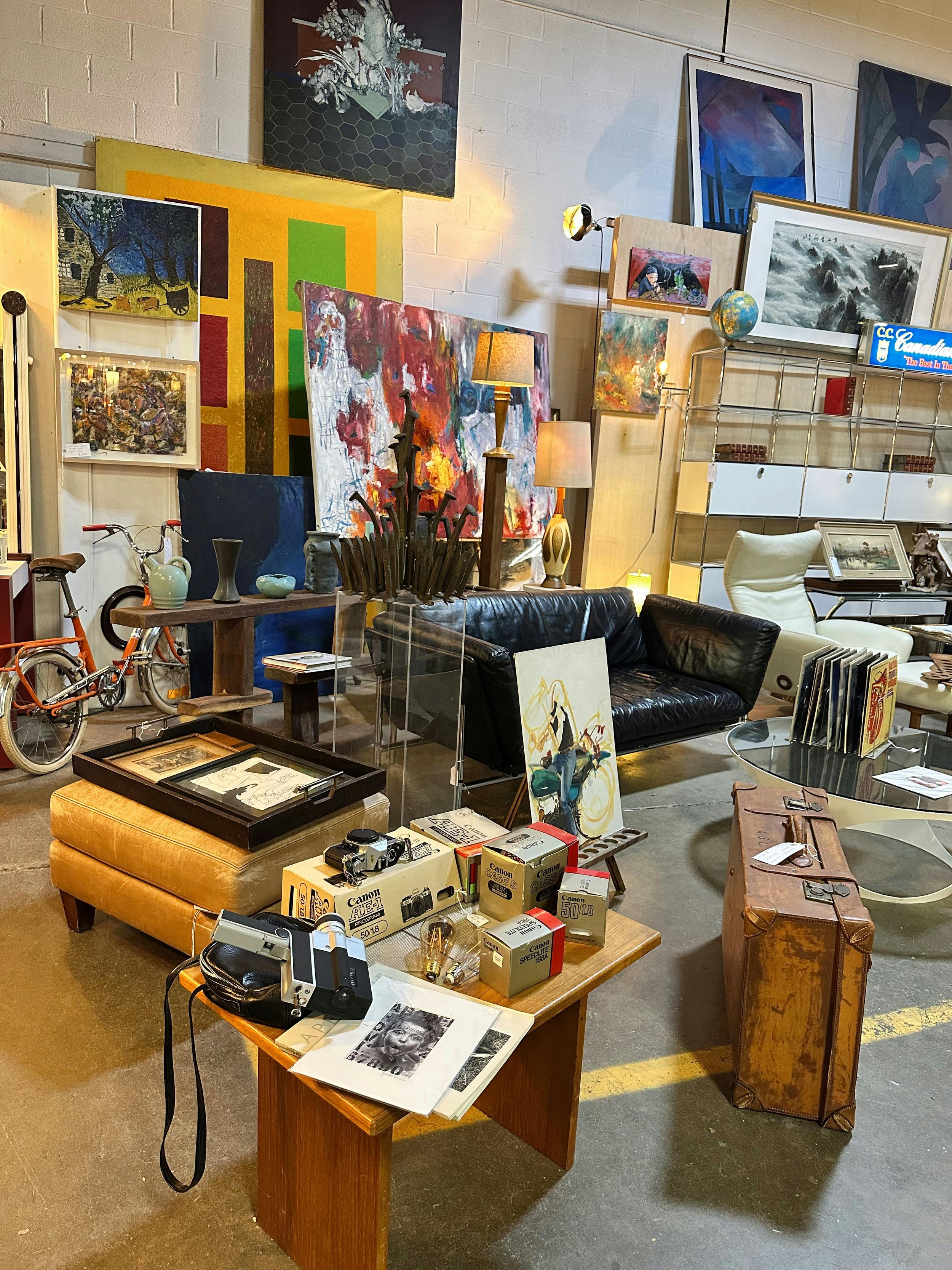 An antique store filled with vintage furniture, artworks on the walls, and various collectibles including cameras, vases, a bicycle, and lamps.