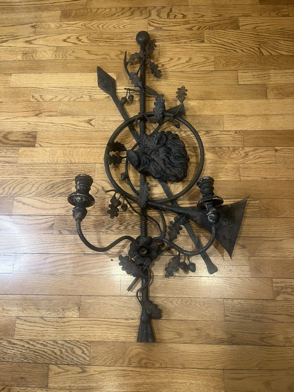 A decorative black metal wall sconce with floral and lion head details, lying on a wooden floor.