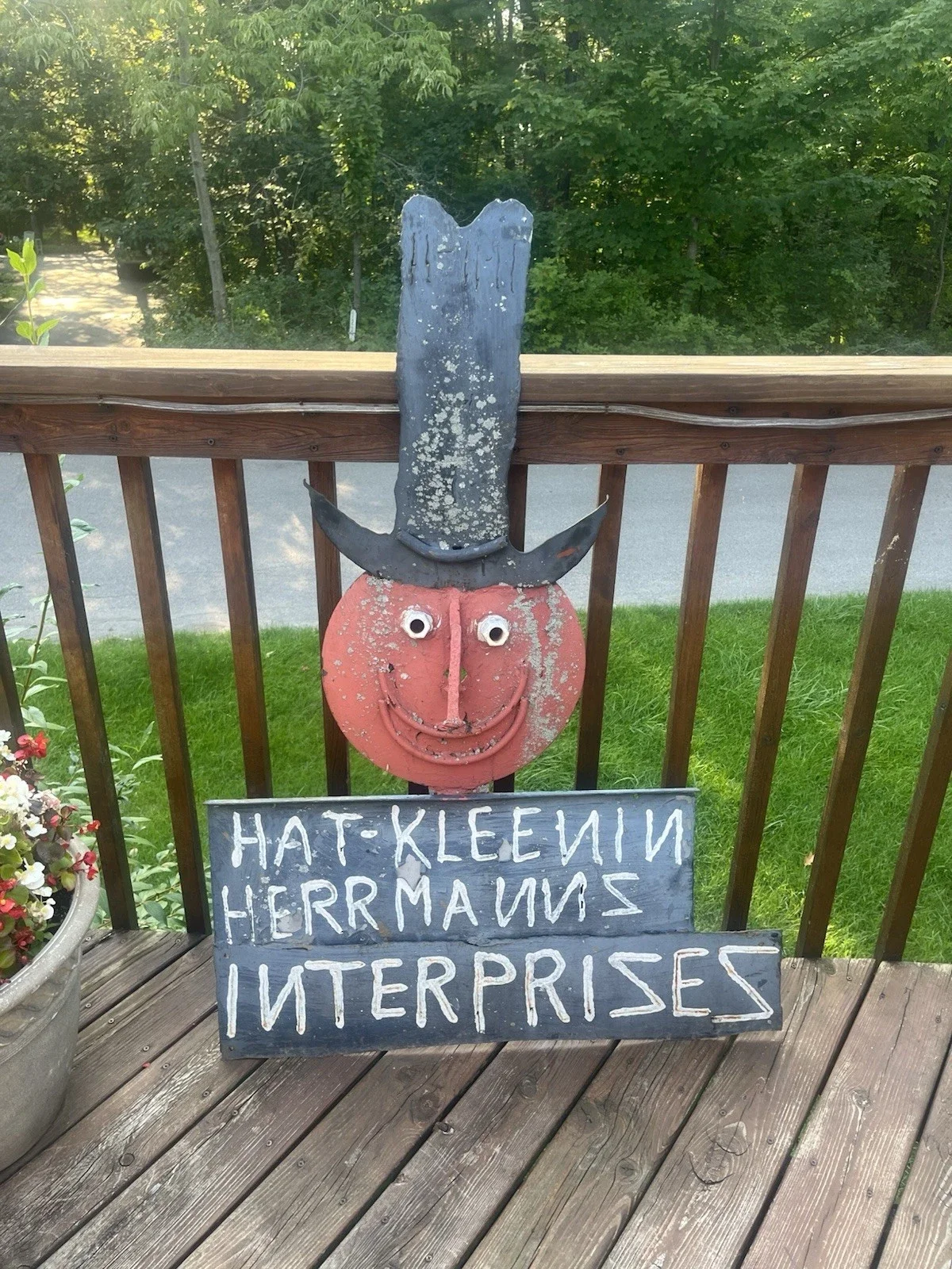 DIY scarecrow decoration on wooden porch with a humorous sign in front.