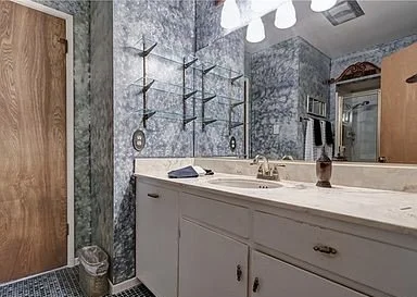 Bathroom with marble walls, white vanity with two sinks, wall-mounted shelves, mirror, and wooden cabinet