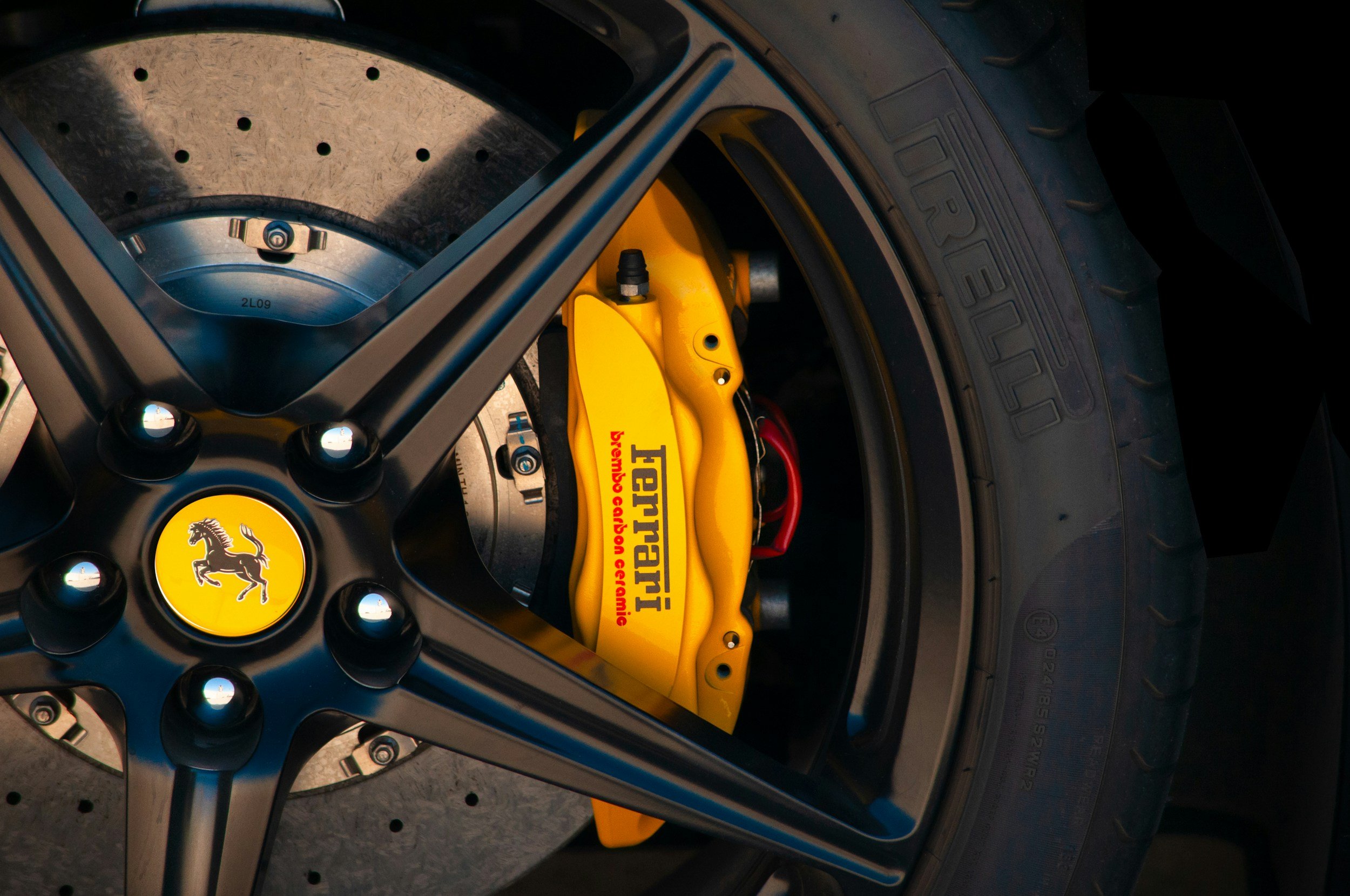 Close-up of a Ferrari wheel featuring a yellow brake caliper with the Ferrari logo, Brembo branding, and ceramic brake disc visible.