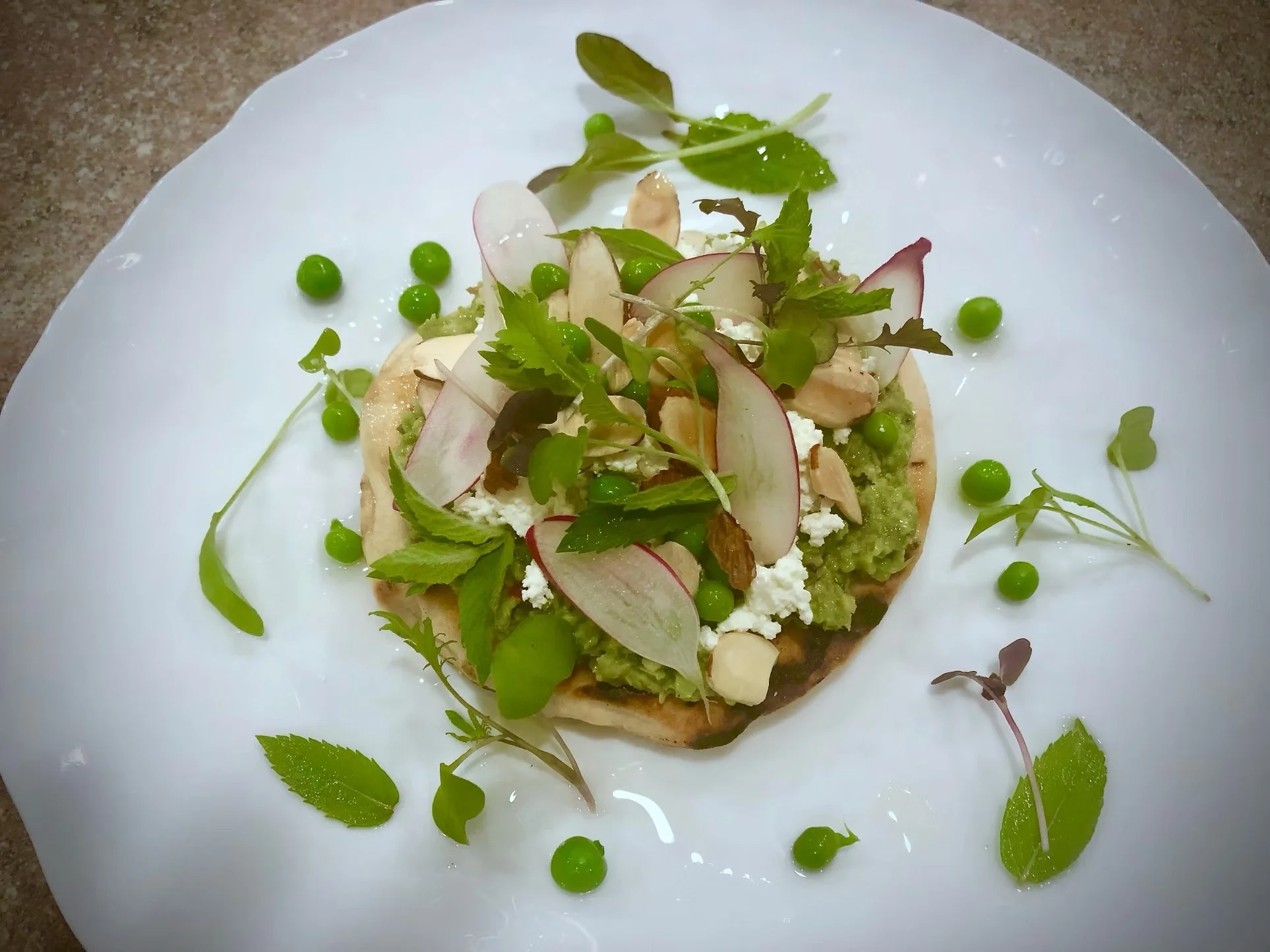 A plate with a vegetable tart topped with sliced radishes, assorted greens, and herbs, garnished with green peas and microgreens.