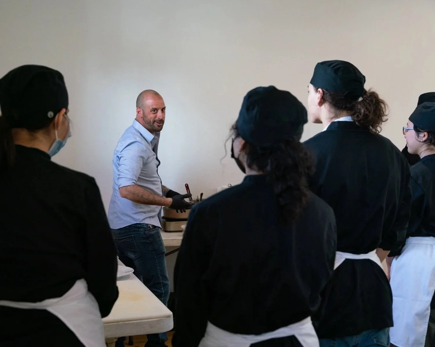 Chef Joe demonstrating cooking techniques to a group of people in a kitchen course.
