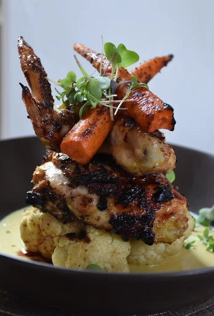 Entree with roasted carrots and microgreens served on cauliflower with sauce in a bowl.