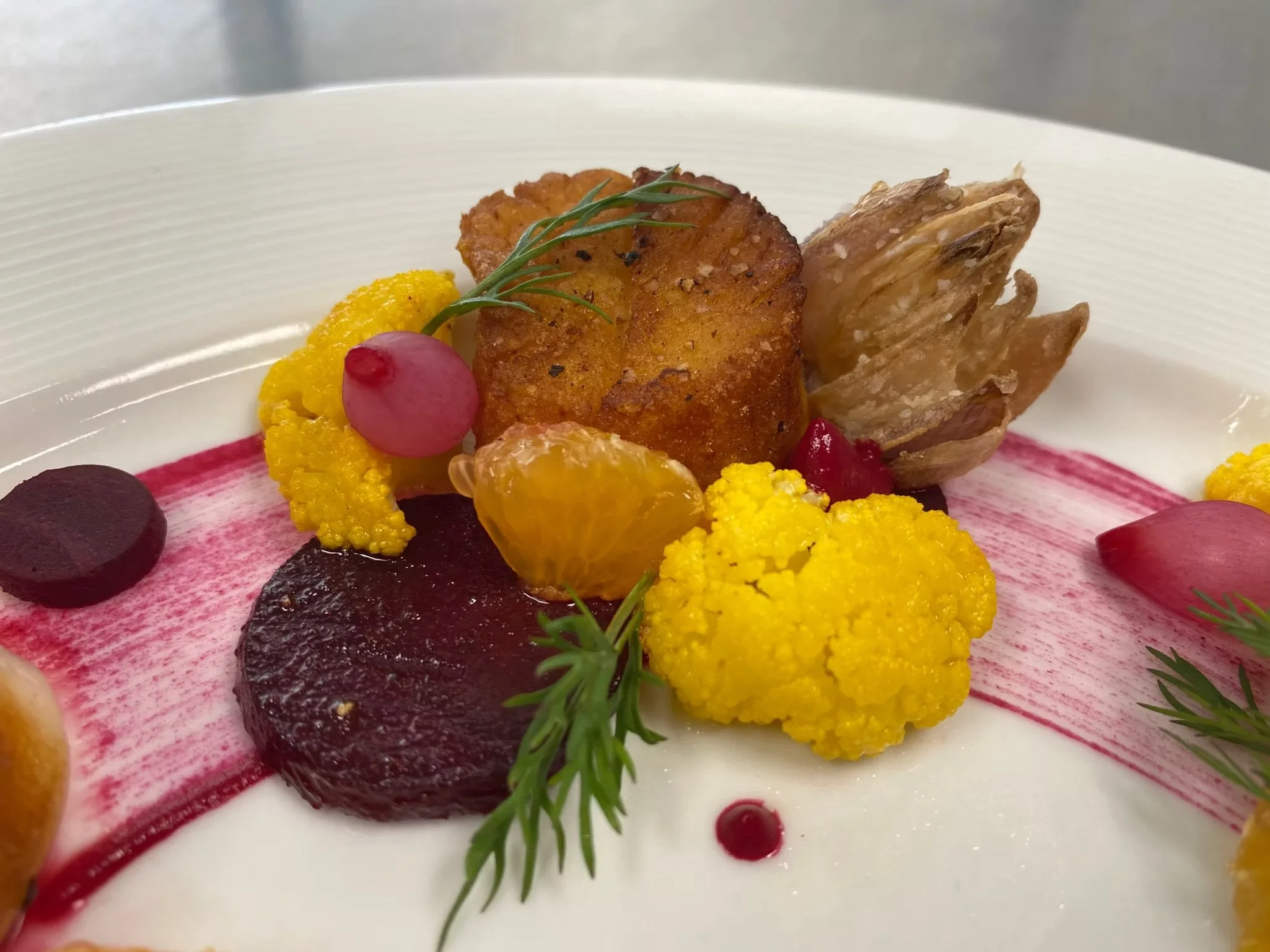 Close-up of a plated dish with colorful vegetables, garnishes, and sauce on a white plate.