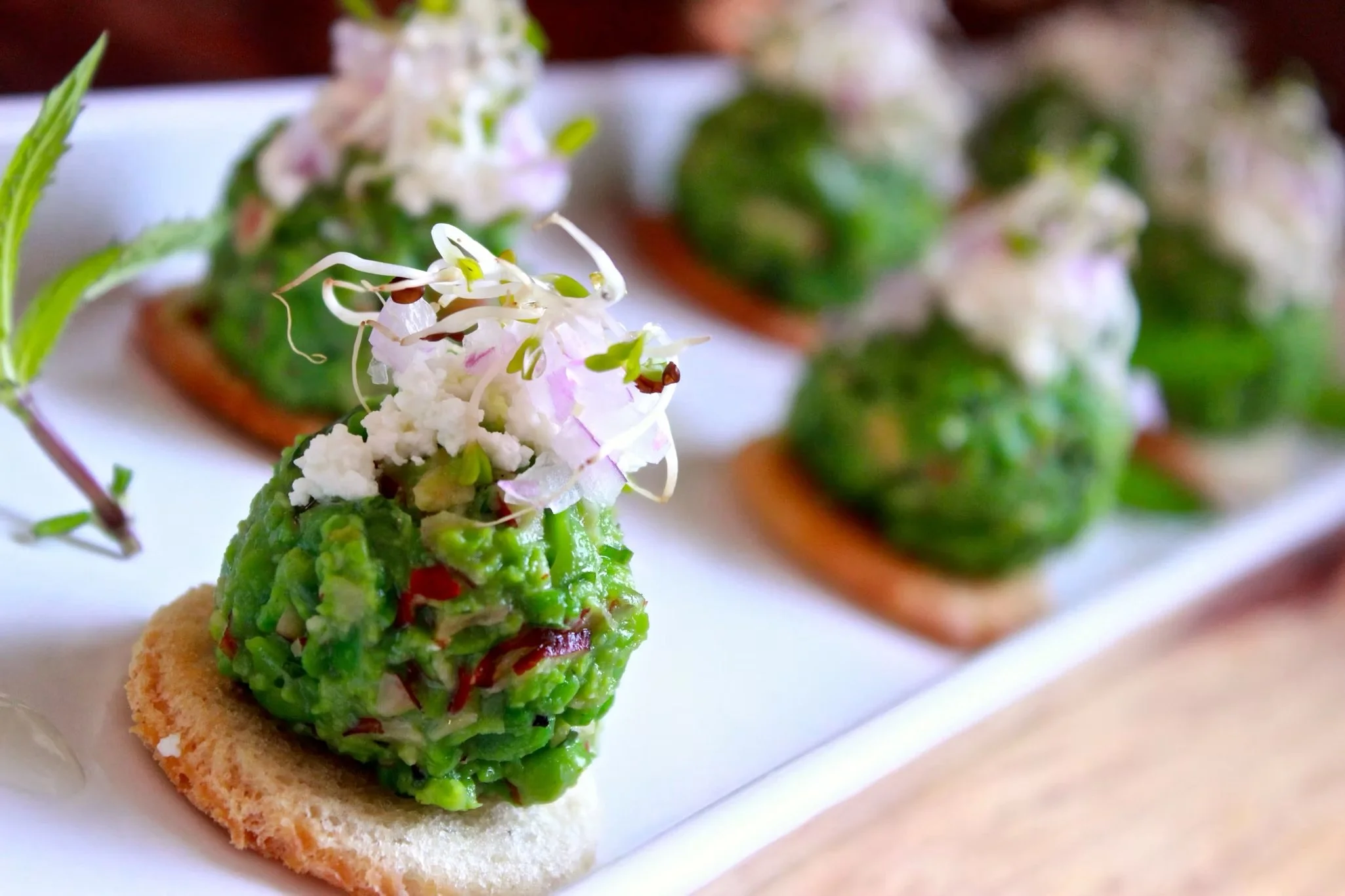 Close-up of gourmet spring appetizer topped with edible flowers on a round cracker, served on a white platter with other similar dishes in the background.