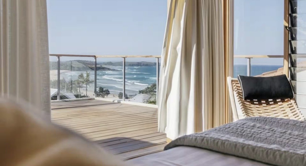 View of the ocean from a balcony, with a bed and curtains partially visible in the foreground.
