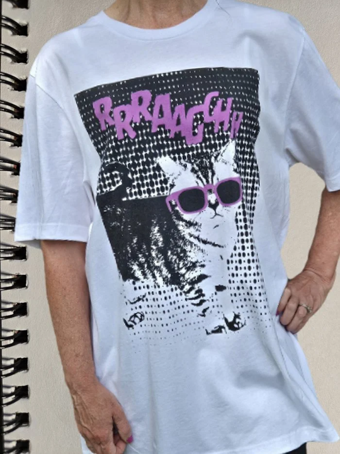 A person wearing a white T-shirt featuring a graphic of a cat with sunglasses, with bold purple text above reading 'RARRAAAGHH'.