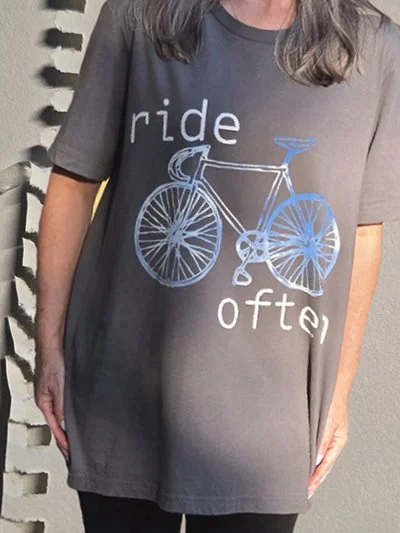 A person wearing a dark gray t-shirt with a blue outline of a bicycle and the words "ride" and "often" printed on it.