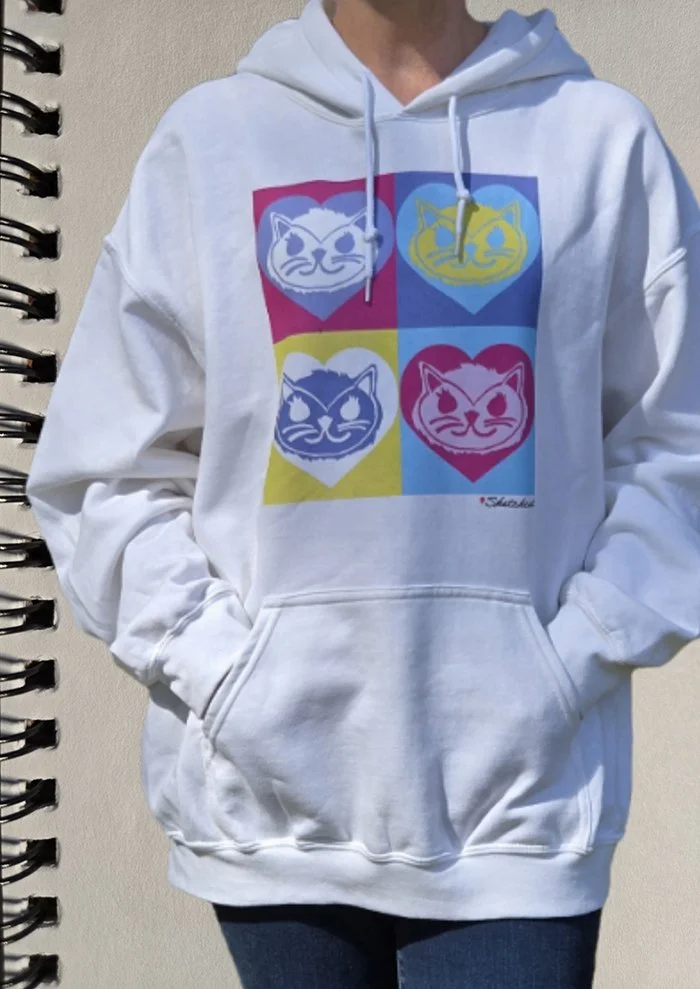 Person wearing a white hoodie with a colorful pop art print of four cartoon cat faces, each in a different color square.