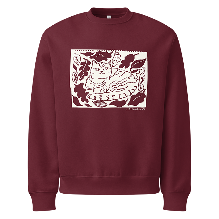 Maroon sweatshirt with a graphic of a cat sitting among leaves and foliage, drawn in a wood cut style.