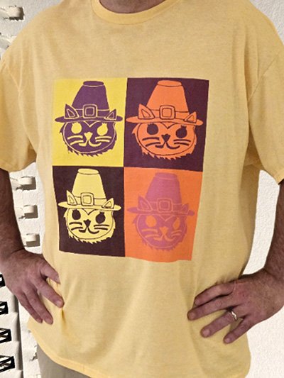 Yellow T-shirt with a pop art design of a cat face wearing a pilgrim hat in four color variations: purple on yellow, orange on purple, white on black, and purple on orange.