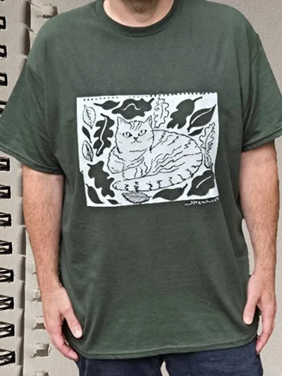 Green T-shirt with a black and white illustrated cat surrounded by leaves and plants.