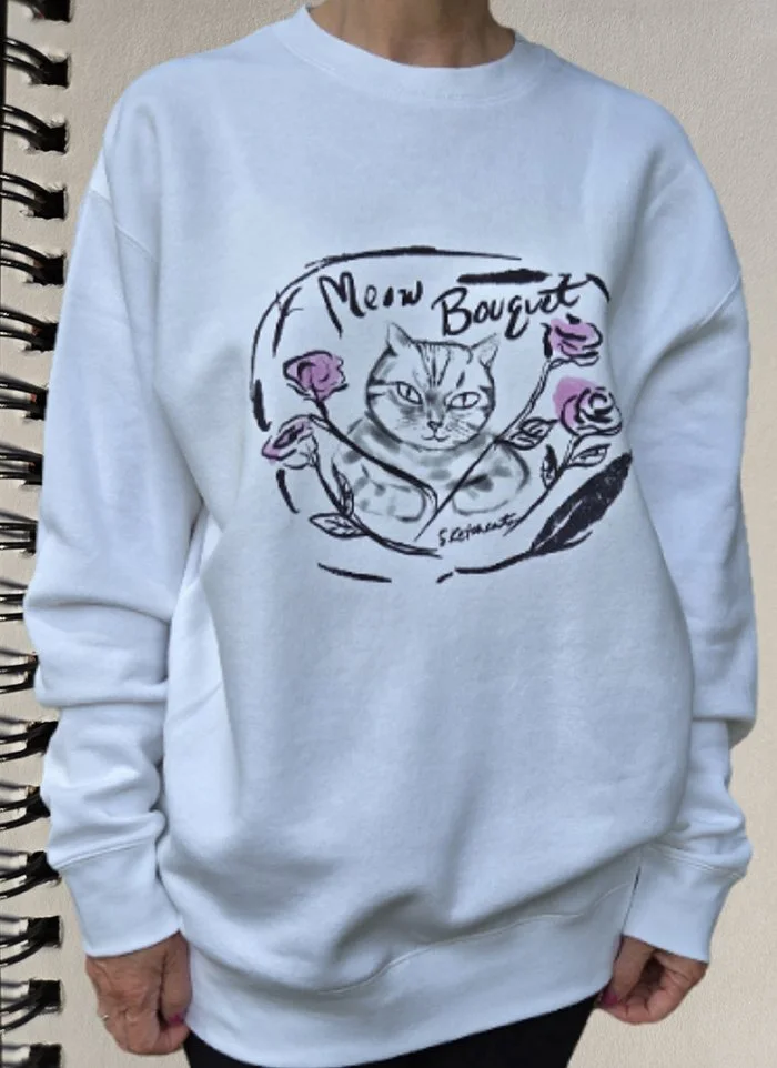 White sweatshirt featuring a sketch of a cat surrounded by pink roses and the words 'Meow Bouquet' in stylized handwriting.