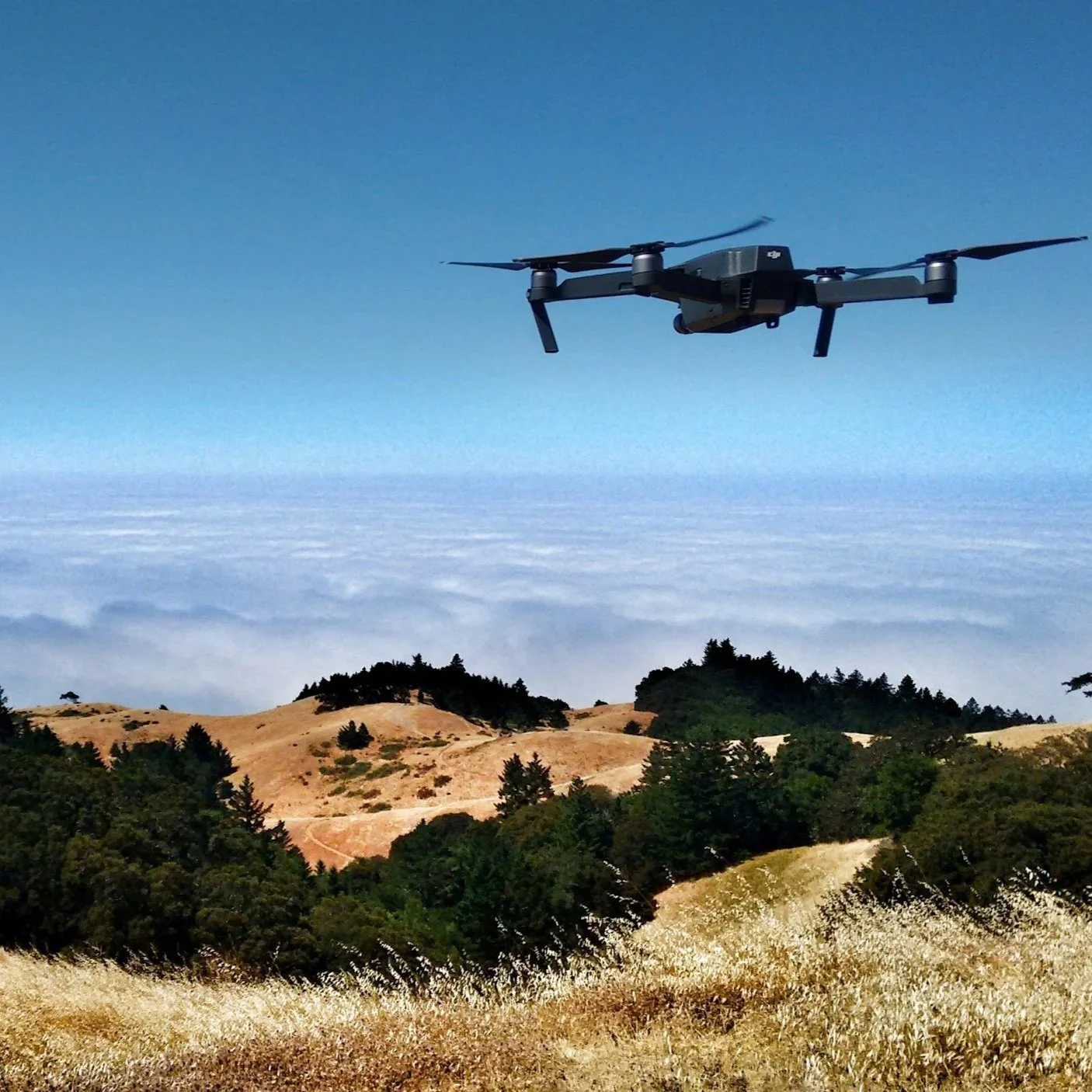 A drone flying over a landscape of rolling hills and trees with a sky filled with clouds in the background.