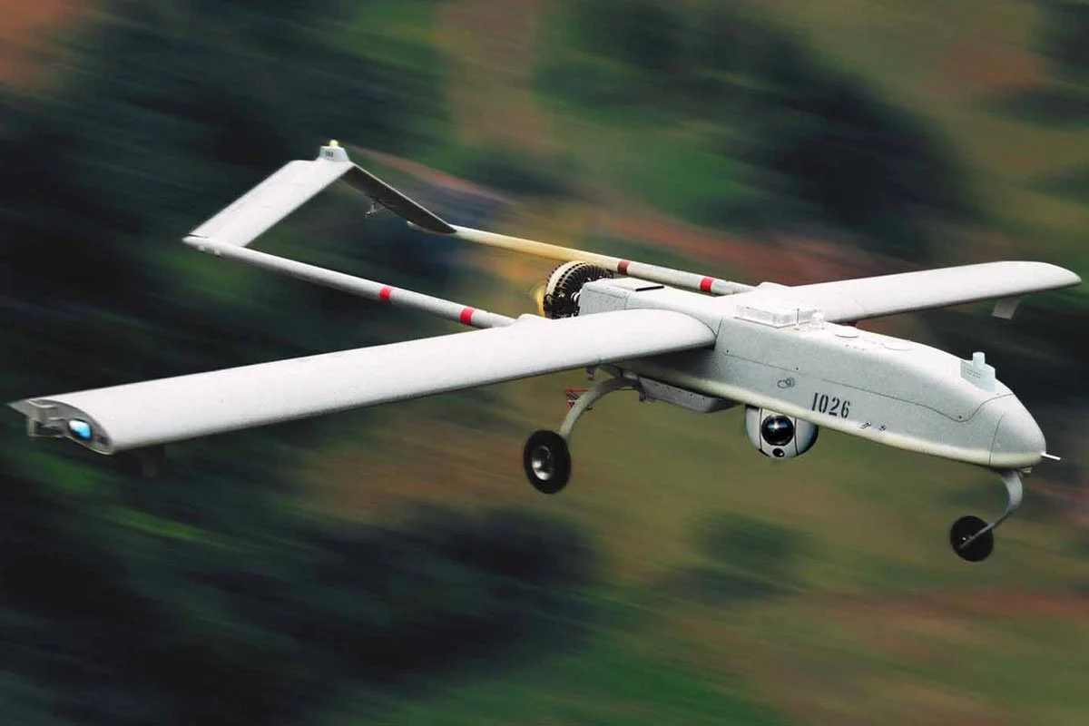 An armed drone flying over a blurred landscape