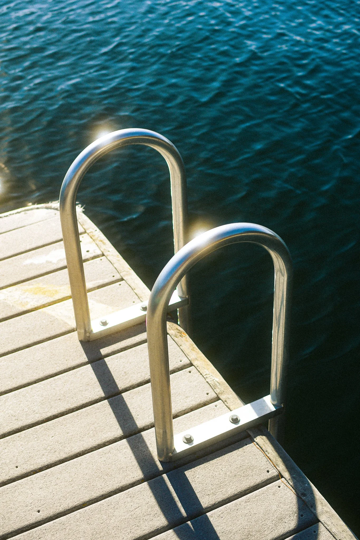 Silver metal boat ladder attached to a dock, with water below.