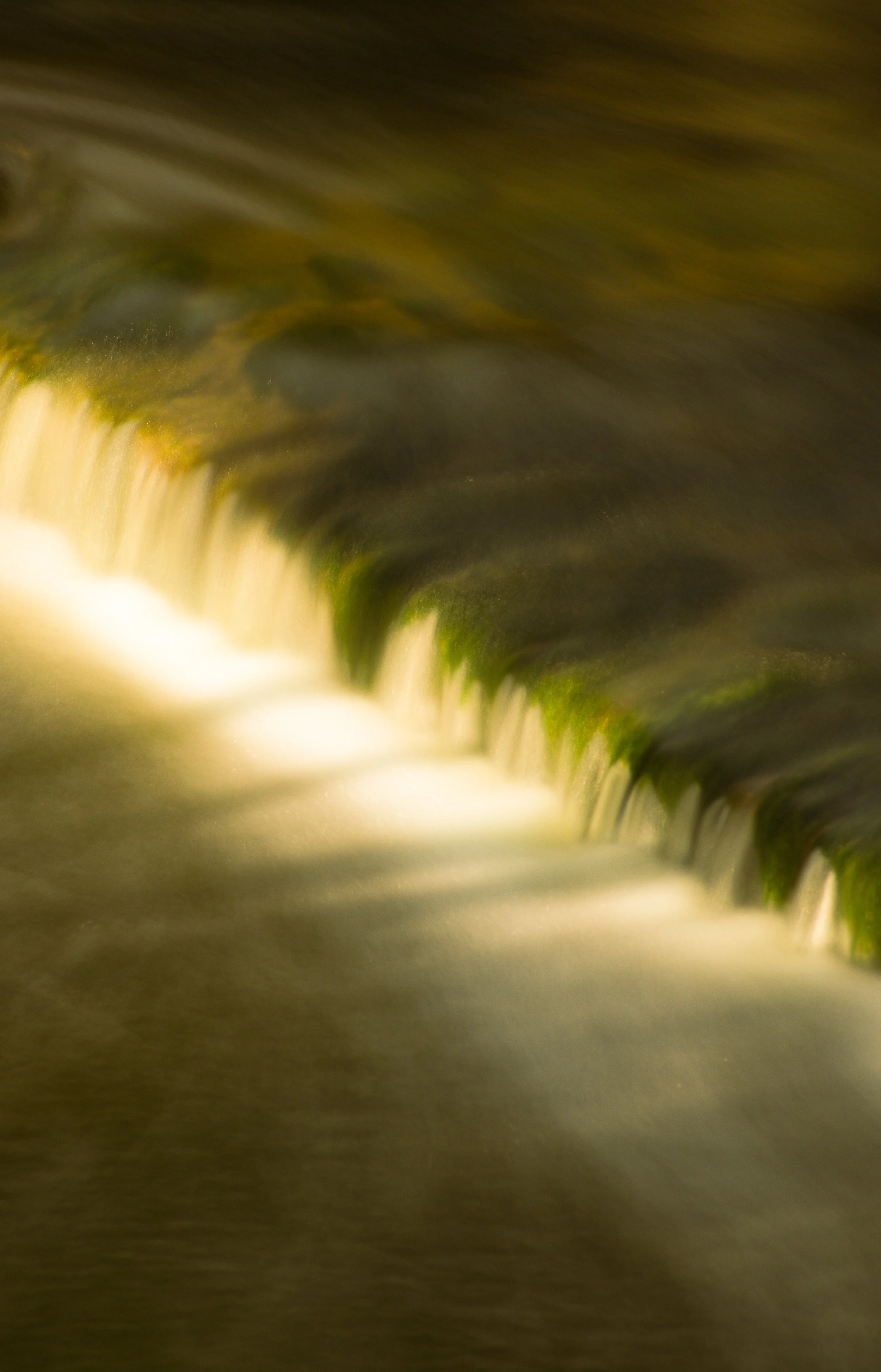 Blurred image of a flowing waterfall, with moss on rocks and water cascading down.