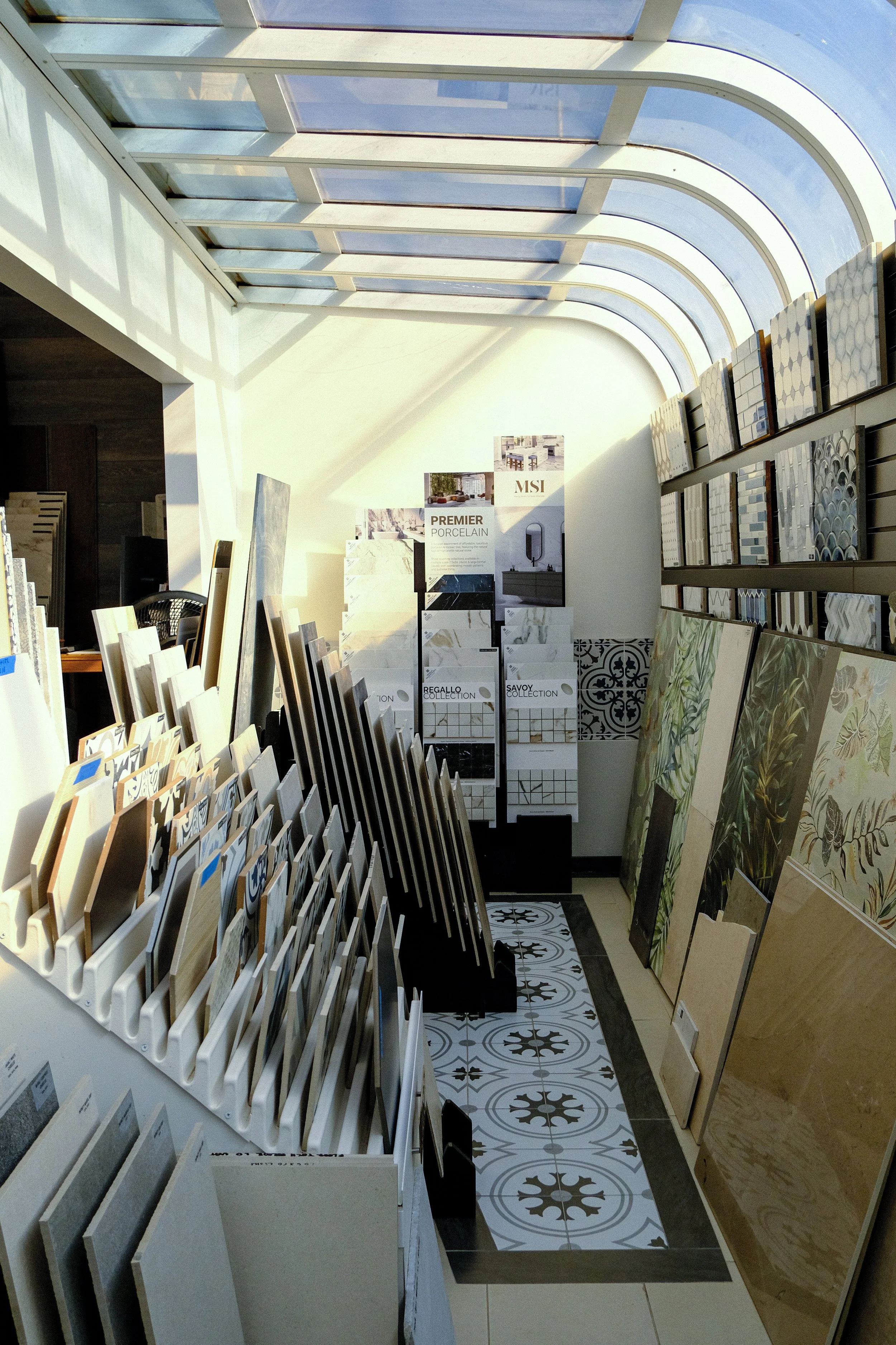 Display of various tile samples in a showroom with natural light from a curved glass ceiling.