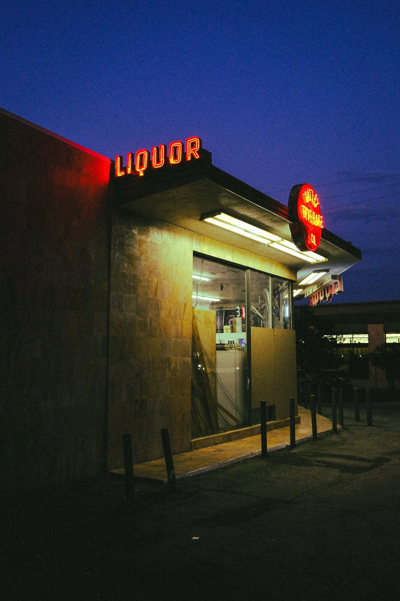 Nighttime exterior of a liquor store with illuminated red neon signs reading 'LIQUOR' and 'SALE'.
