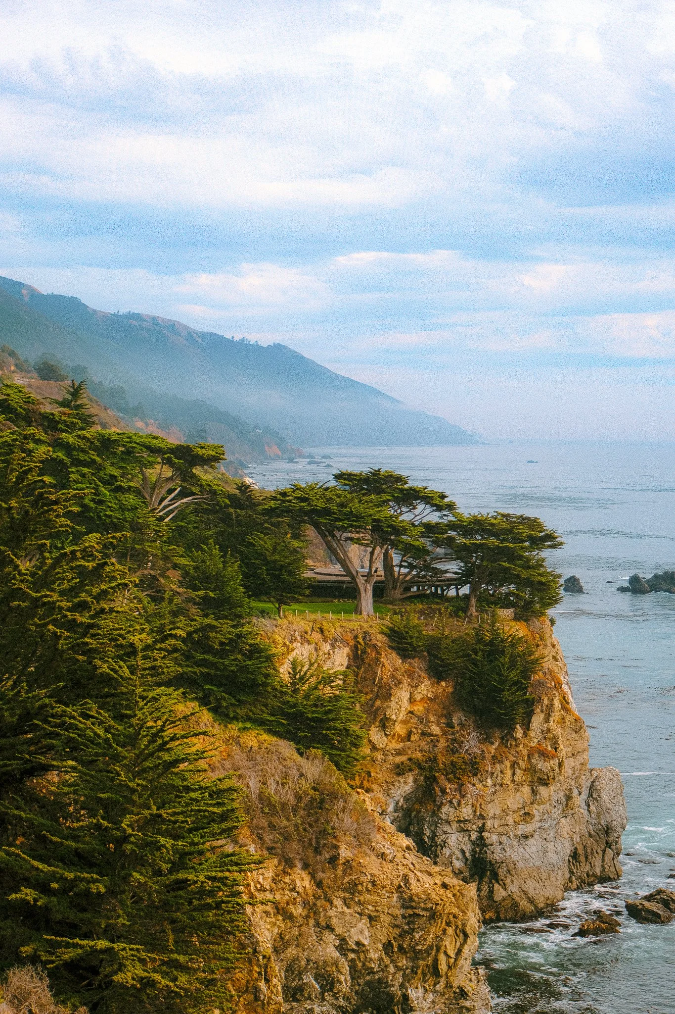 California coast with rocky cliffs, green trees, and ocean view under cloudy sky