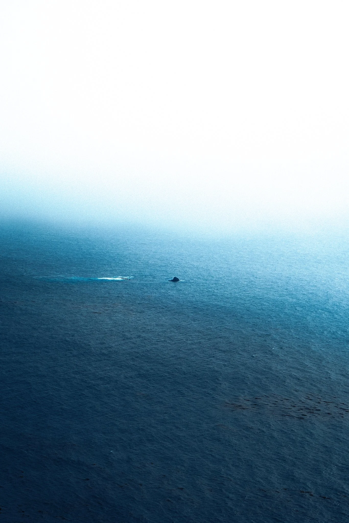 Ocean with a small rock or island and a boat or ship seen from a distance.