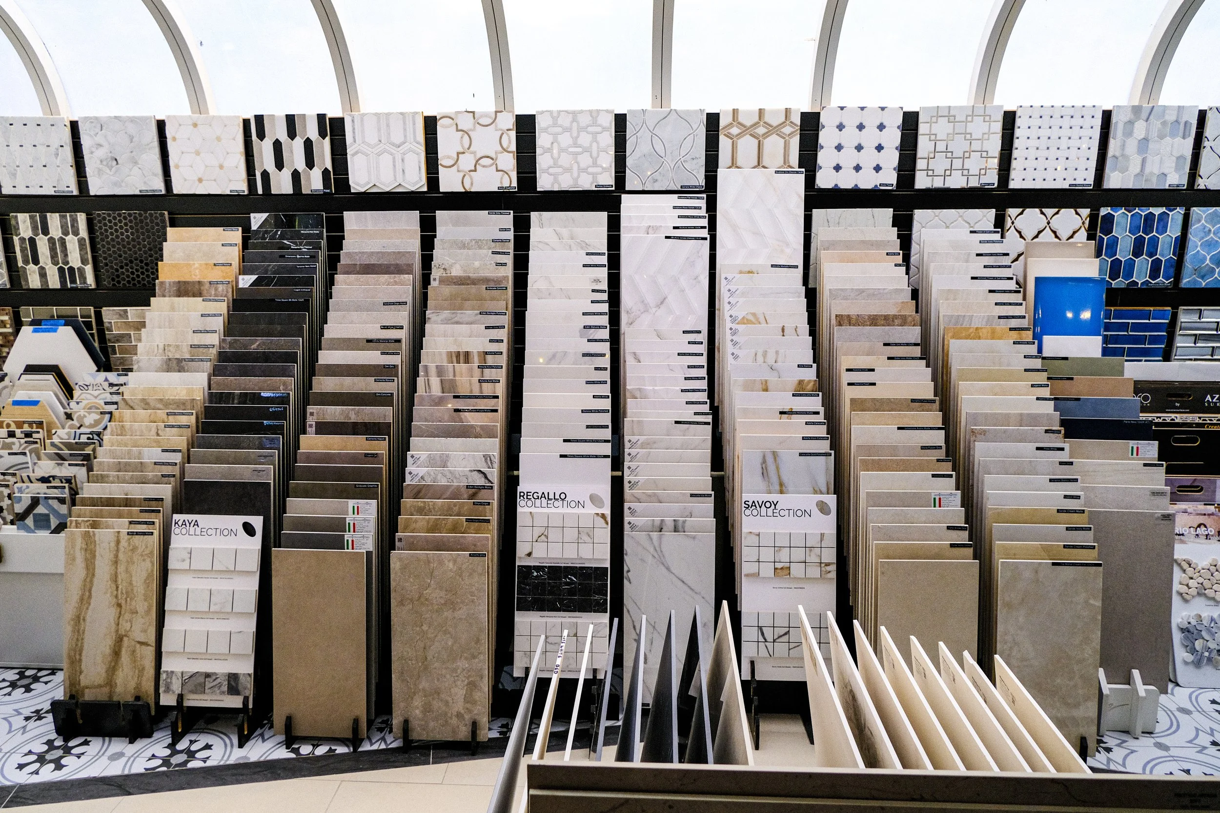 Displays a variety of tile samples in different colors and patterns arranged in vertical rows at a store.