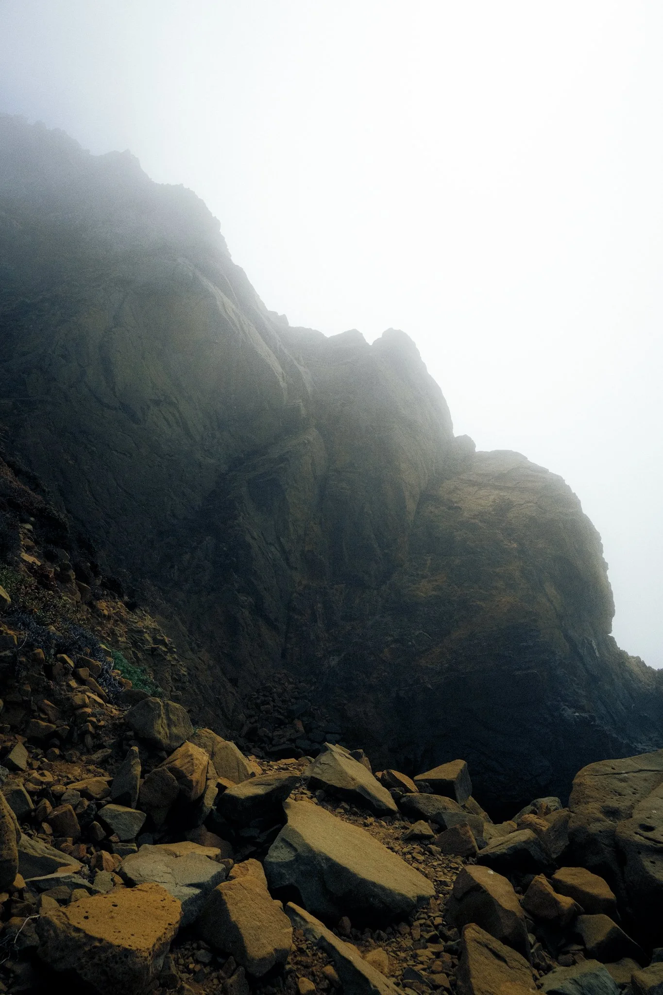 A foggy mountain landscape with large rocks and boulders at the base of a steep, dark cliff.