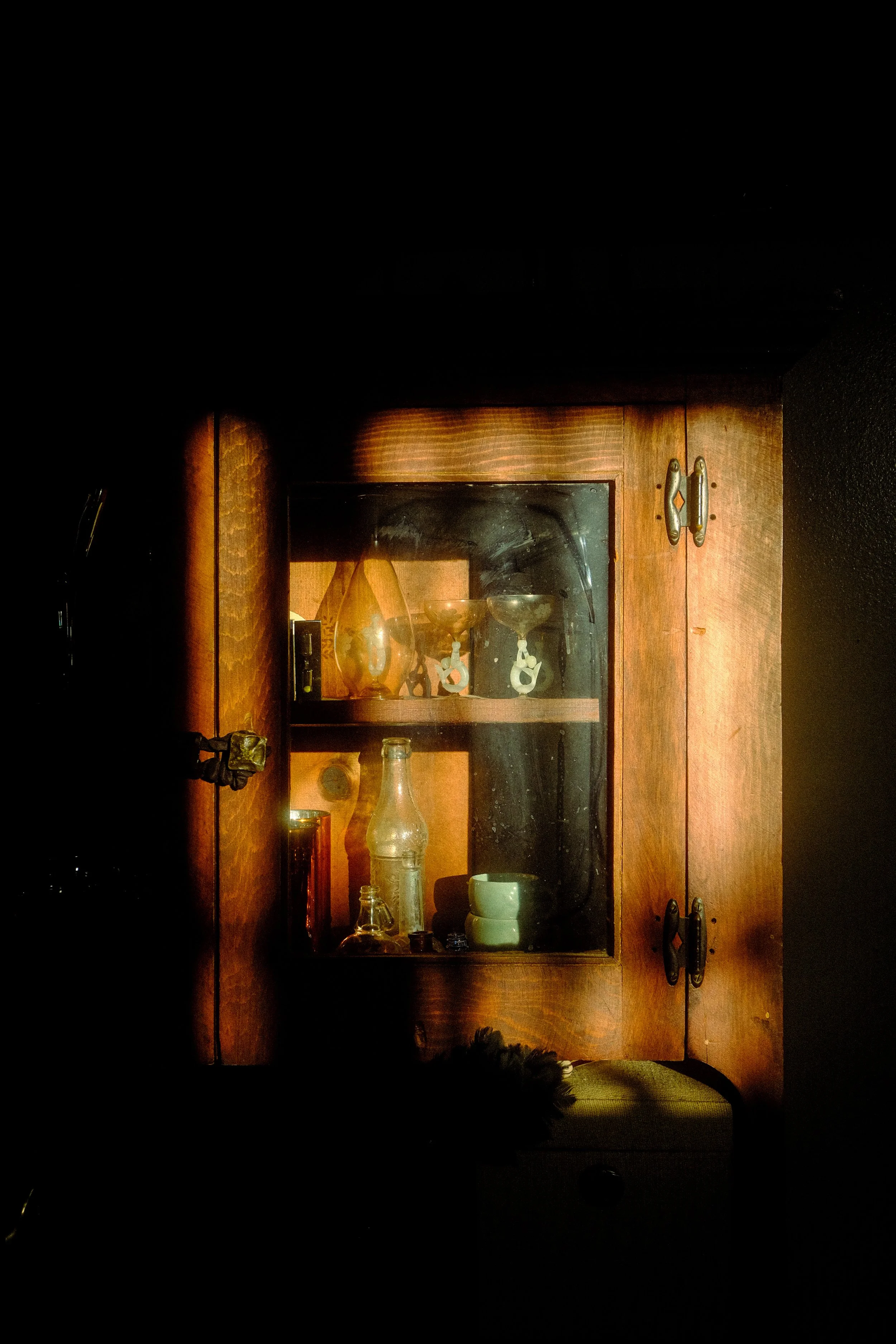A wooden cabinet with glass doors displaying various glassware and small objects, illuminated by warm light.