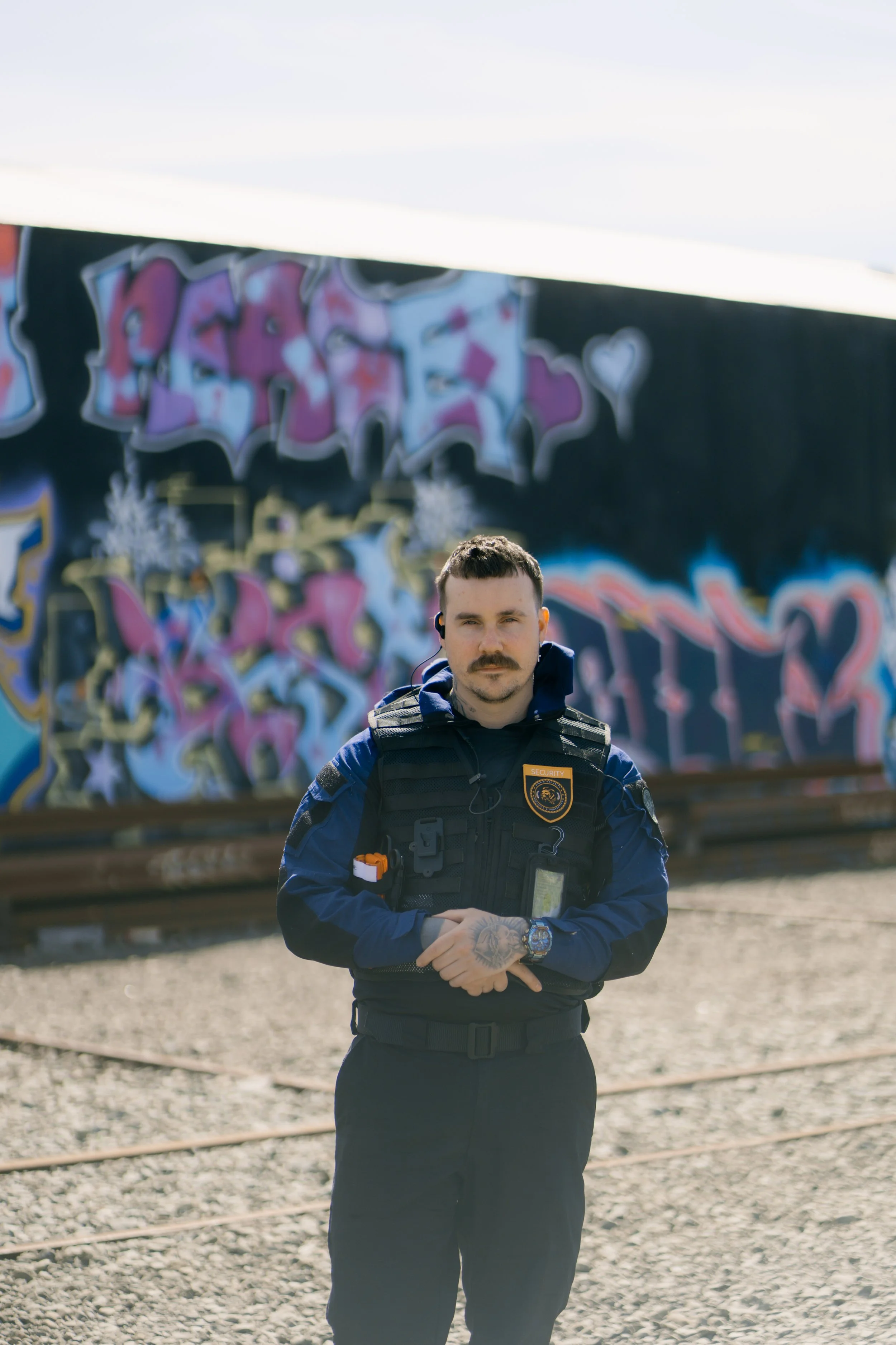 A security officer standing outdoors in front of a graffiti-covered wall.