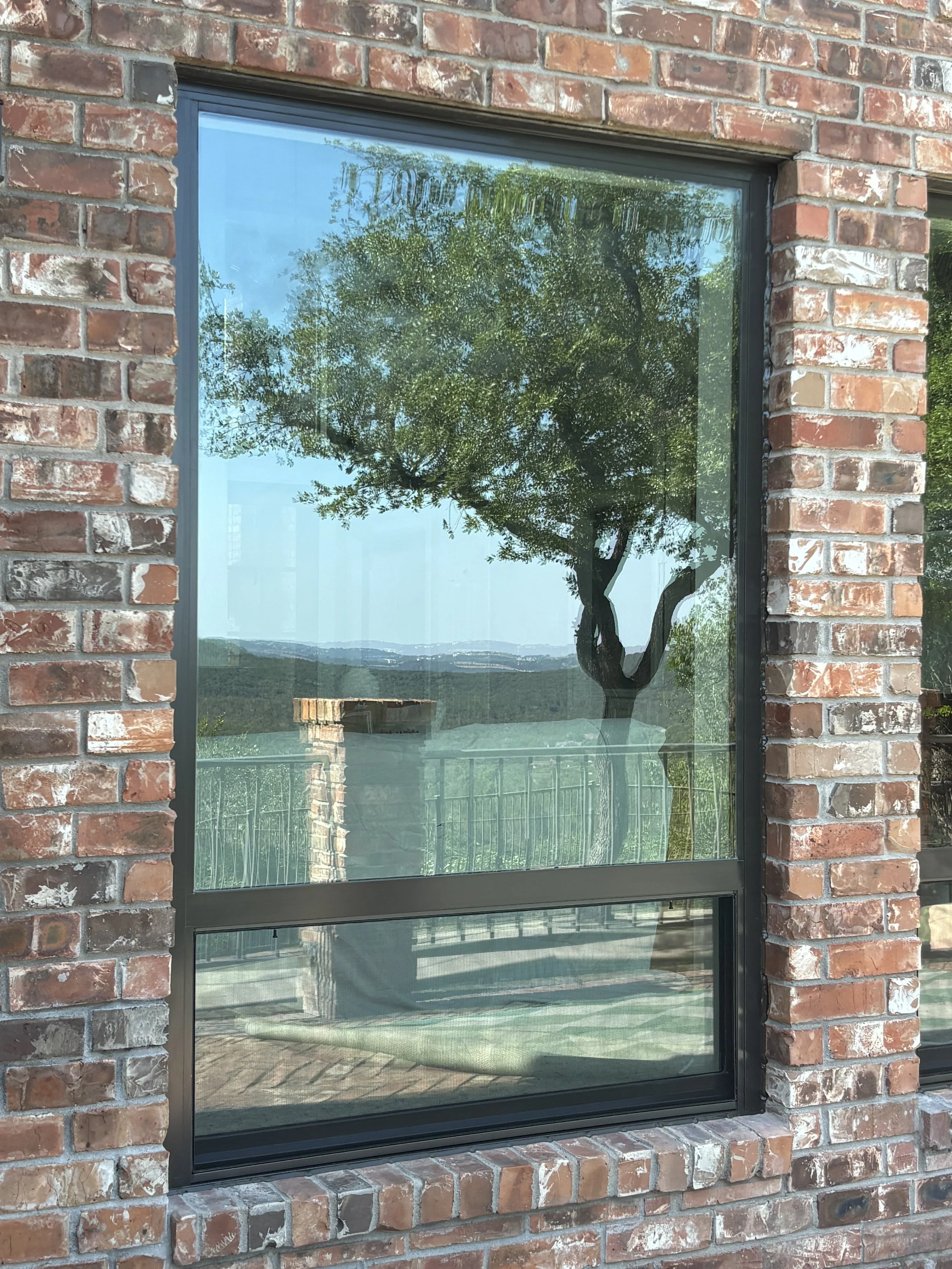 Reflective window on brick building showing a tree and sky outside.