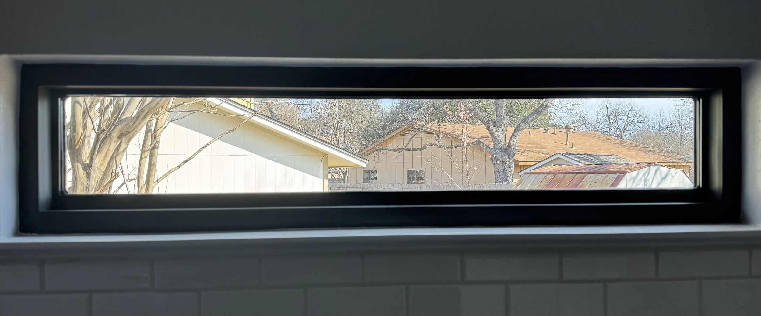 View through a rectangular window showing neighboring houses with trees outside.