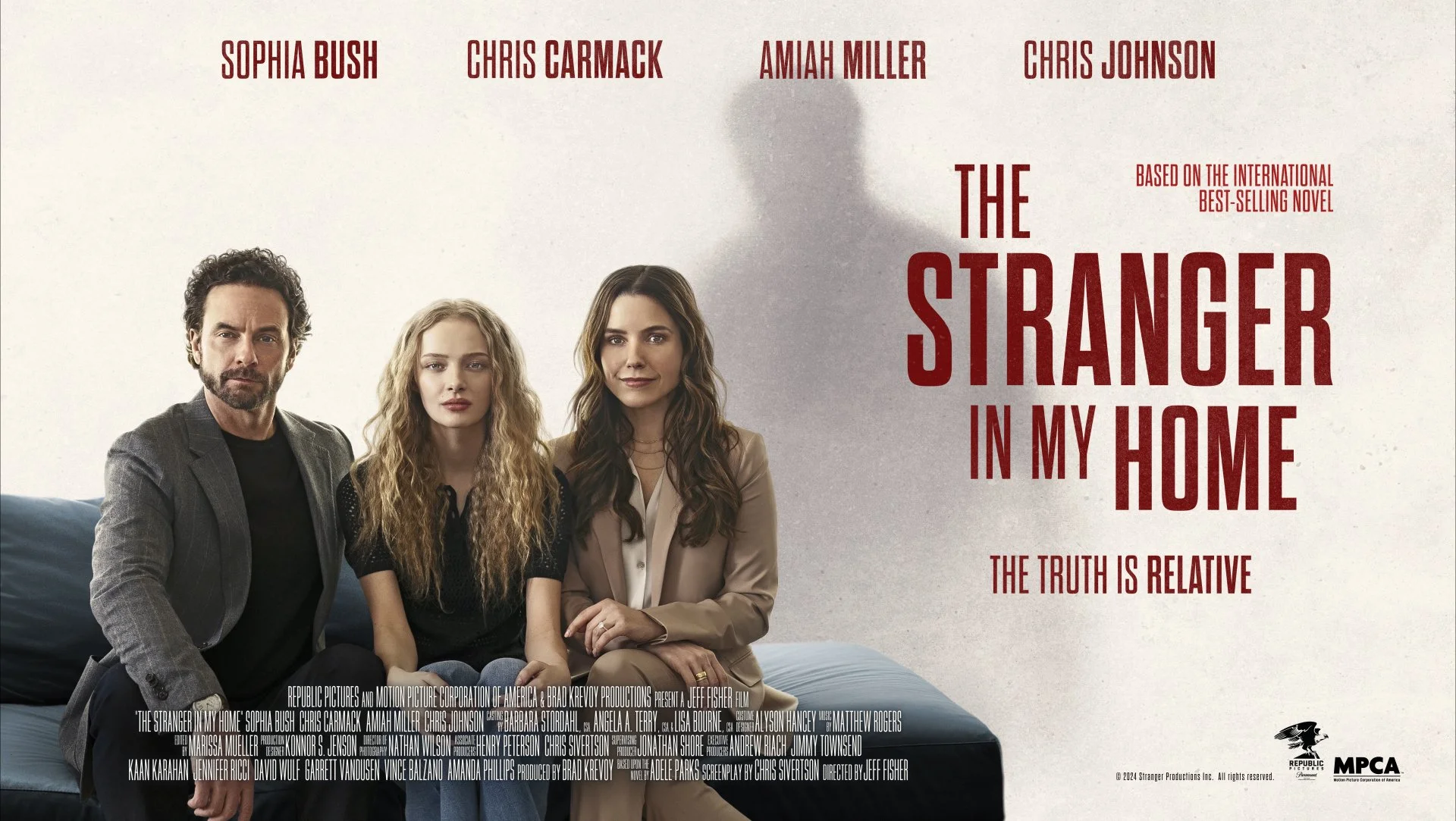 Promotional poster for the movie 'The Stranger in My Home' featuring three people sitting on a couch: a man with dark curly hair and beard wearing a gray blazer, a young woman with long curly blonde hair in a black top, and a woman with long brown ha