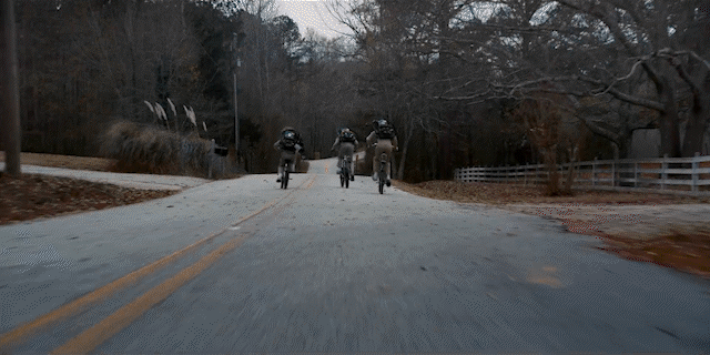 Four cyclists riding on a rural road surrounded by trees in late fall or winter. Stranger Things on Netflix