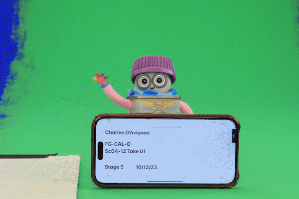A puppet with big eyes, purple hat, and colorful arm waves behind a smartphone displaying a script or scene details, against a green screen background. Tiny Chef.