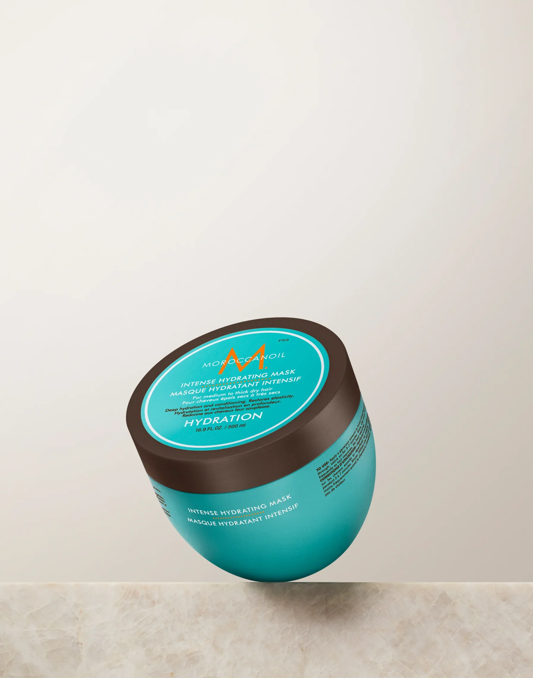 Round container of Morocco Oil Intense Hydrating Mask on black fabric surface.