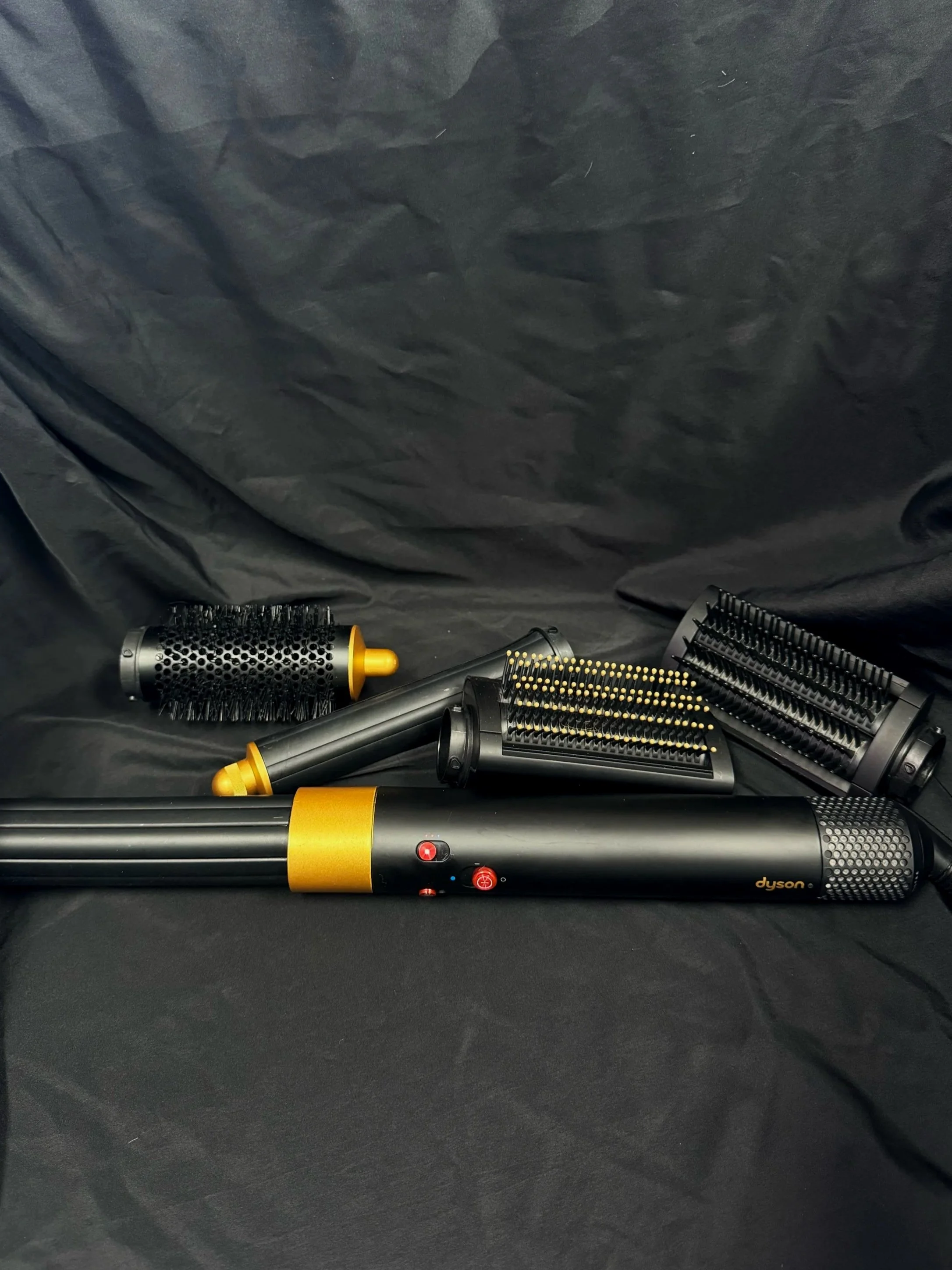 Dyson hair styling tool with multiple interchangeable brush heads on a black surface.