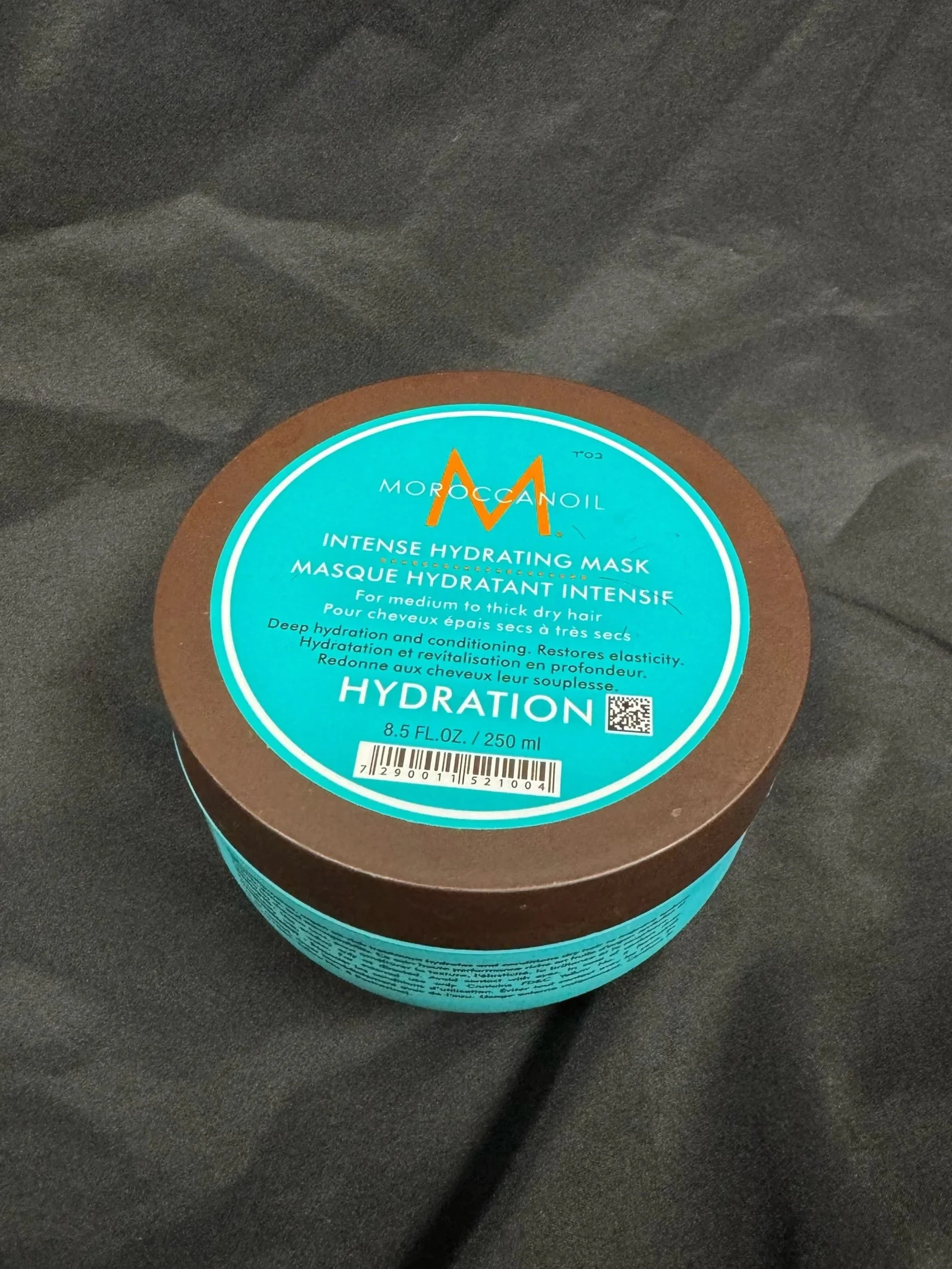Round container of Morocco Oil Intense Hydrating Mask on black fabric surface.